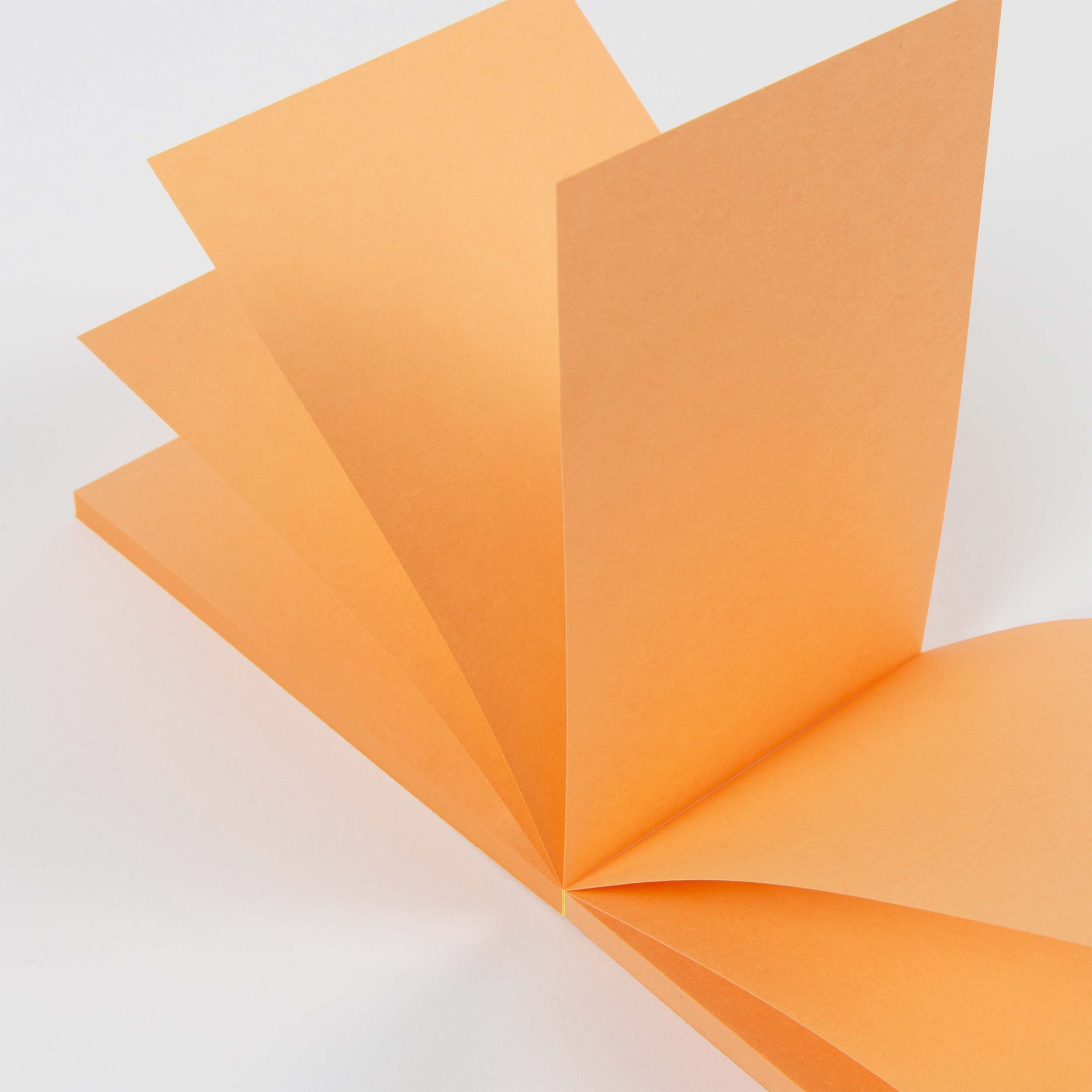 Ein aufgeschlagener Abreissblöcke Neon Notizblock von paperlux aus Feinstpapier-Resten, mit aufgefächerten Neonseiten und von oben betrachtet auf einem schlichten weißen Hintergrund.