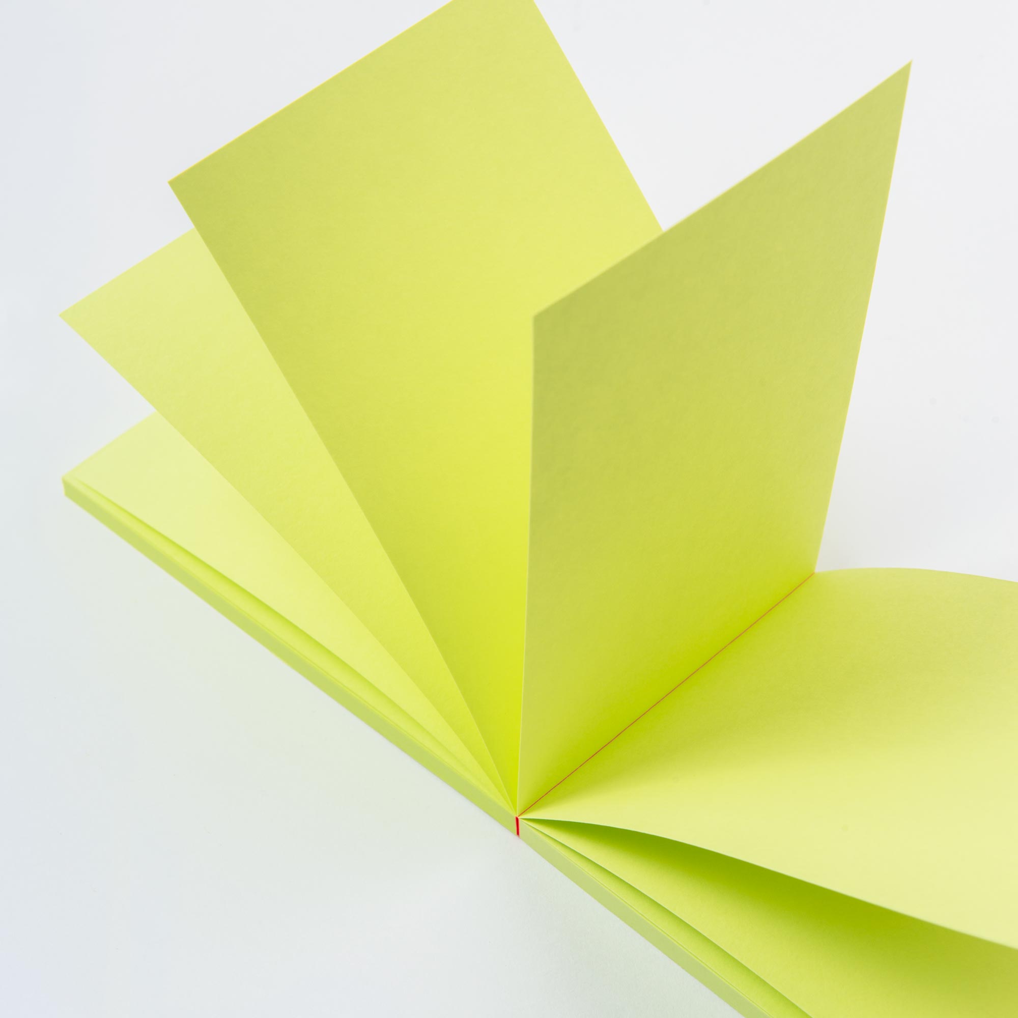 Nahaufnahme eines aufgeschlagenen paperlux Abreissblöcke Neon-Notizbuchs, dessen leuchtend gelbe Feinstpapier-Reste vor einem weißen Hintergrund aufgefächert sind.