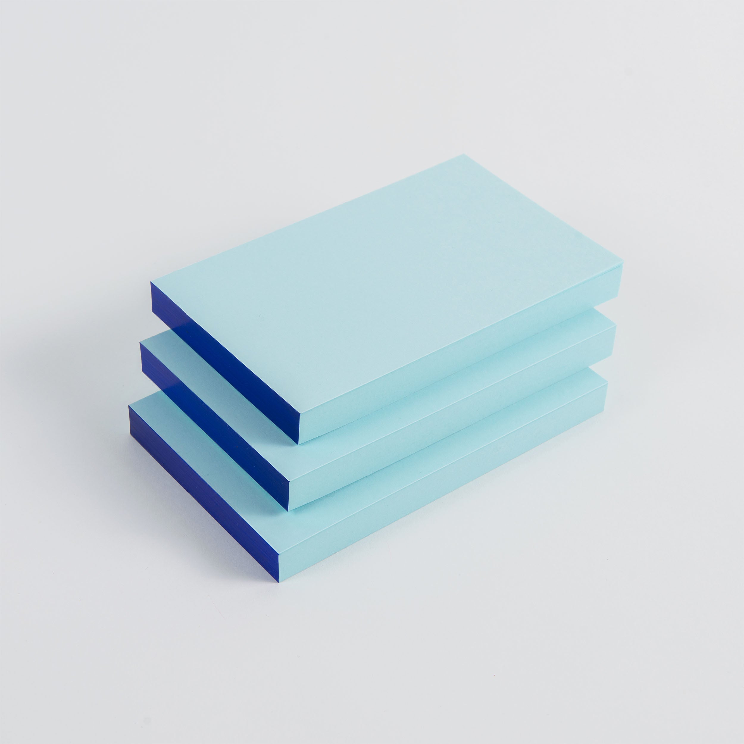 Drei gestapelte, blaugrüne Abreissblöcke Neon von paperlux.store liegen auf einer weißen Oberfläche. Die Blockränder sind dunkelblau, wodurch ein auffälliger Randkontrast entsteht. Hergestellt aus Feinstpapier-Reste, variiert die Farbauswahl passend zu Ihrem Stil.