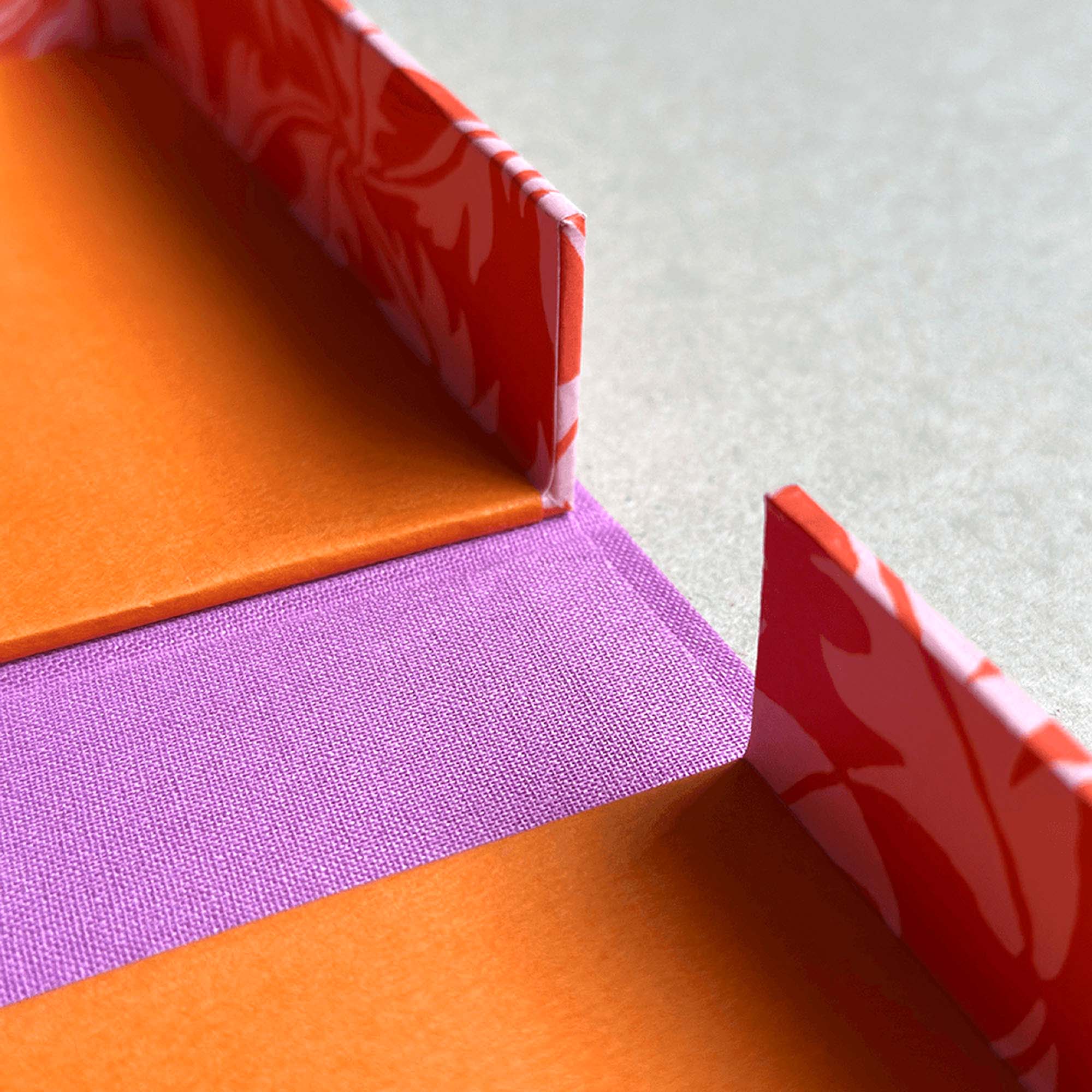 Nahaufnahme von orangefarbenem, rosafarbenem und lilafarbenem Origamipapier mit gemusterten roten und weißen Rändern, die sauber in parallelen Reihen auf einer hellen Fläche angeordnet sind und die Präzision des Workshops Clamshell Box von paperlux.store widerspiegeln.