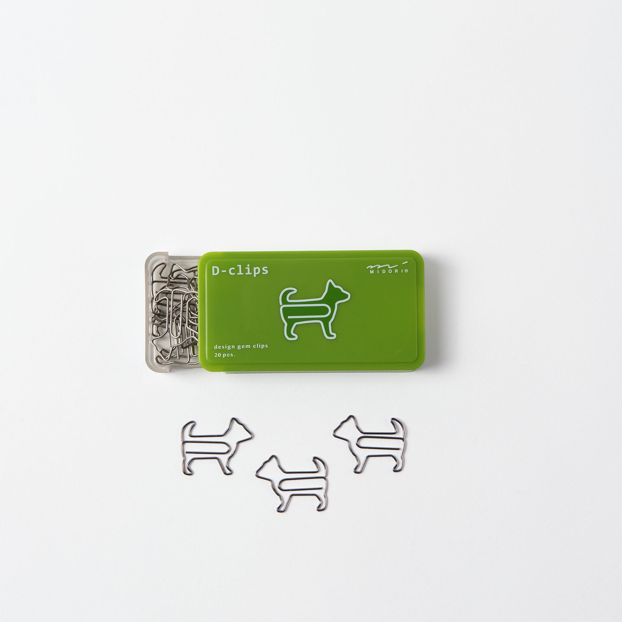 Eine hübsche grüne Schachtel mit der Aufschrift „D-Clips: Büroklammern Hund“ von Midori, Japan, enthält hundeförmige Büroklammern, geöffnet auf weißem Hintergrund. Drei dieser entzückenden Büroklammern sind ordentlich neben der Schachtel angeordnet.