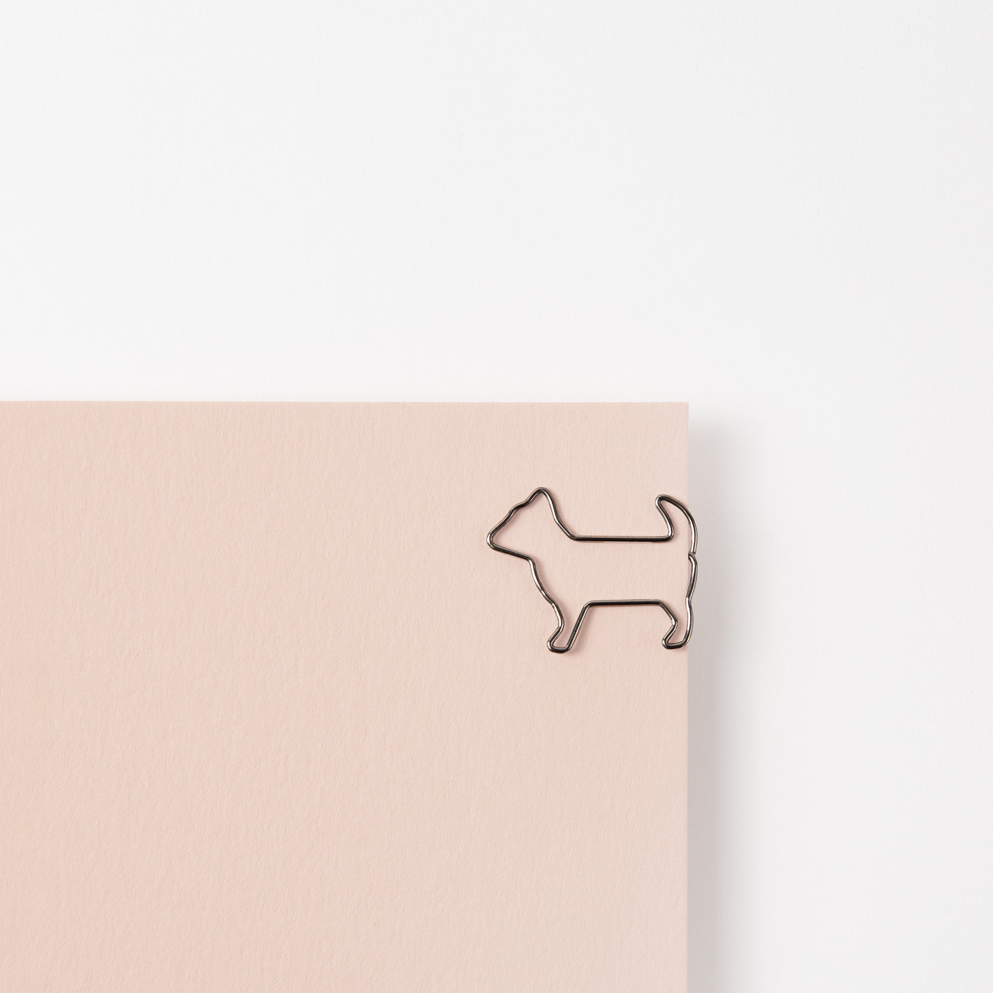 Ein beiges Blatt Papier zeigt in der oberen rechten Ecke einen niedlichen Clip in Form eines Hundes namens Midori D-Clips: Büroklammern Hund. Der schlichte weiße Hintergrund bietet eine minimalistische Ästhetik mit einem Hauch japanischen Einflusses.