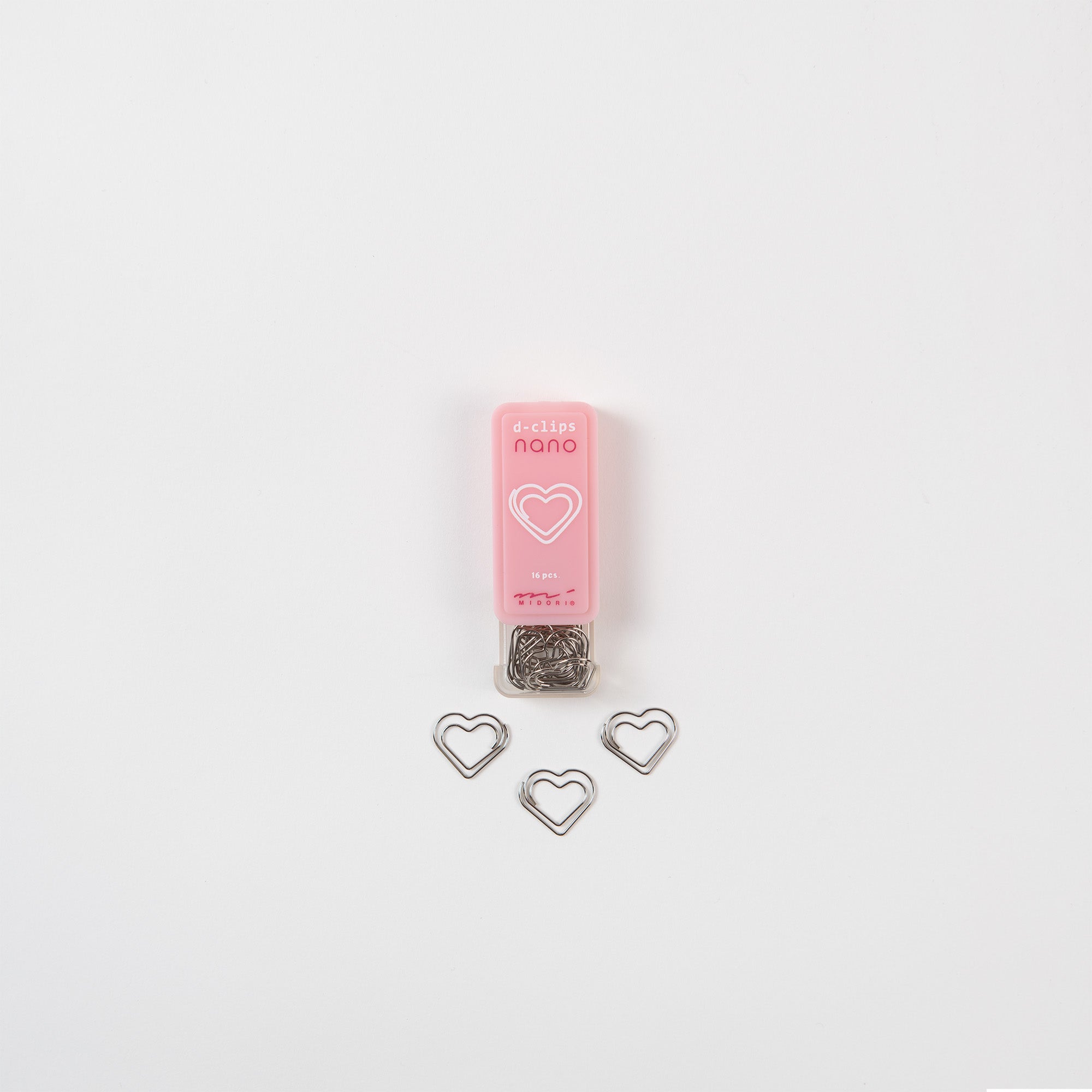 Der Midori „D-Clips Nano: Herzen für Alle“ ist ein kleiner rosa Behälter mit Herzmotiven, perfekt zum Ordnen von Notiz- oder Liebesbriefen. Er enthält silberne herzförmige Clips, wobei drei Clips außen auf einem makellos weißen Hintergrund platziert sind und so für einen eleganten Zusammenhalt sorgen.