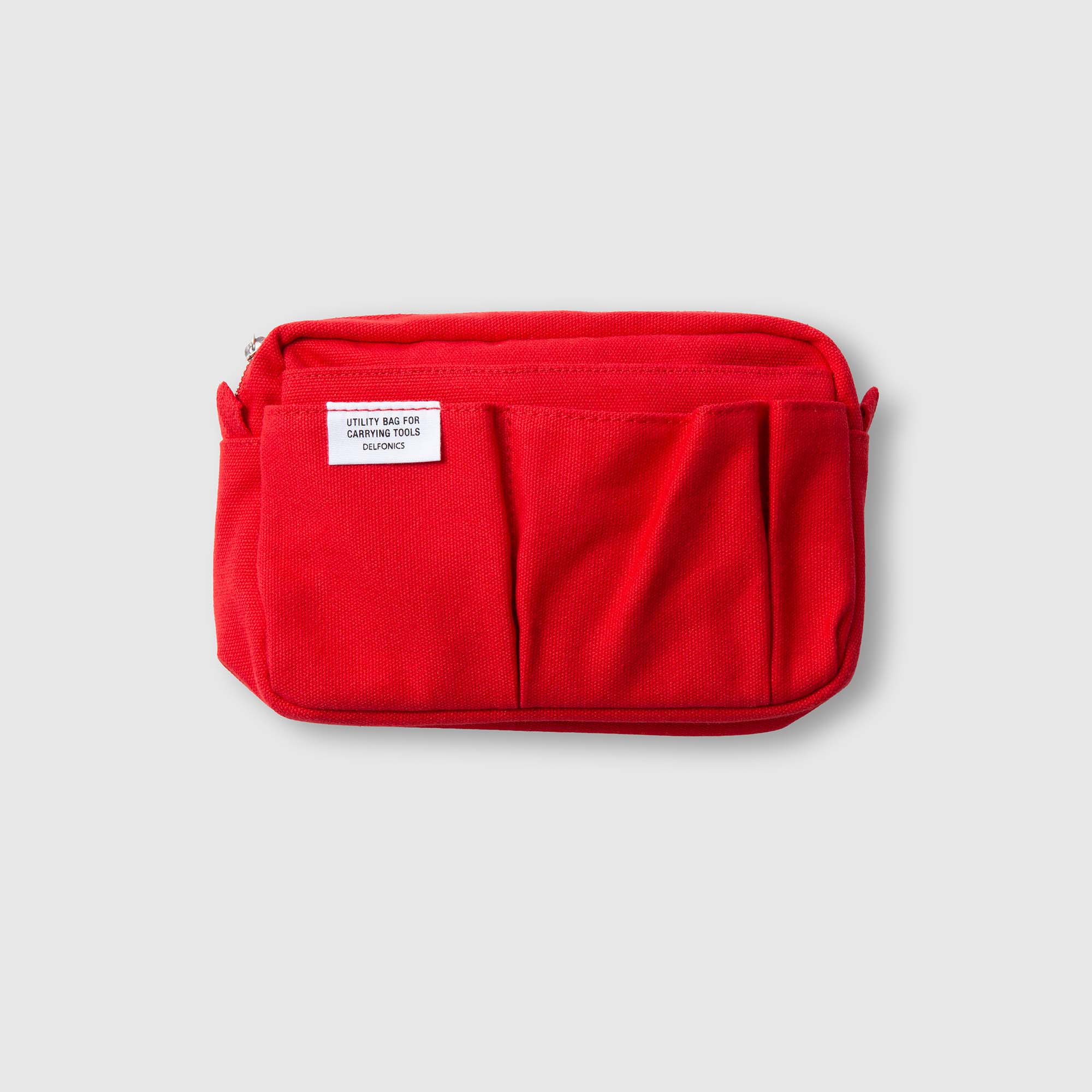 Eine kompakte rote „Delfonics Inner Carrying Bag S“ von Delfonics, die dem originalen „Inner Carrying Case“ nachempfunden ist, verfügt über mehrere Fronttaschen und ein charakteristisches weißes Etikett. Vor einem schlichten hellgrauen Hintergrund fotografiert, eignet sie sich perfekt als Organizer-Tasche oder praktische Baumwolltasche für Ihre Alltagsutensilien.