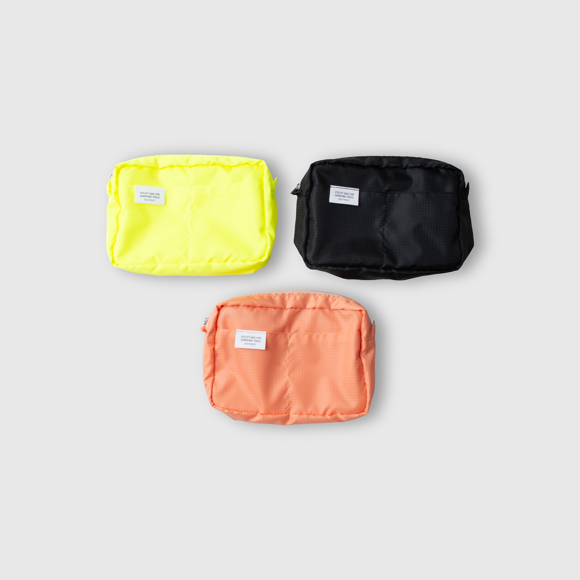 Drei „Delfonics Inner Carrying Case AIR S“-Taschen in den Farben Gelb, Schwarz und Pfirsich – jeweils aus strapazierfähigem Ripstop-Gewebe gefertigt und mit einem kleinen weißen Etikett versehen – sind auf hellgrauem Hintergrund in Dreiecksform angeordnet.