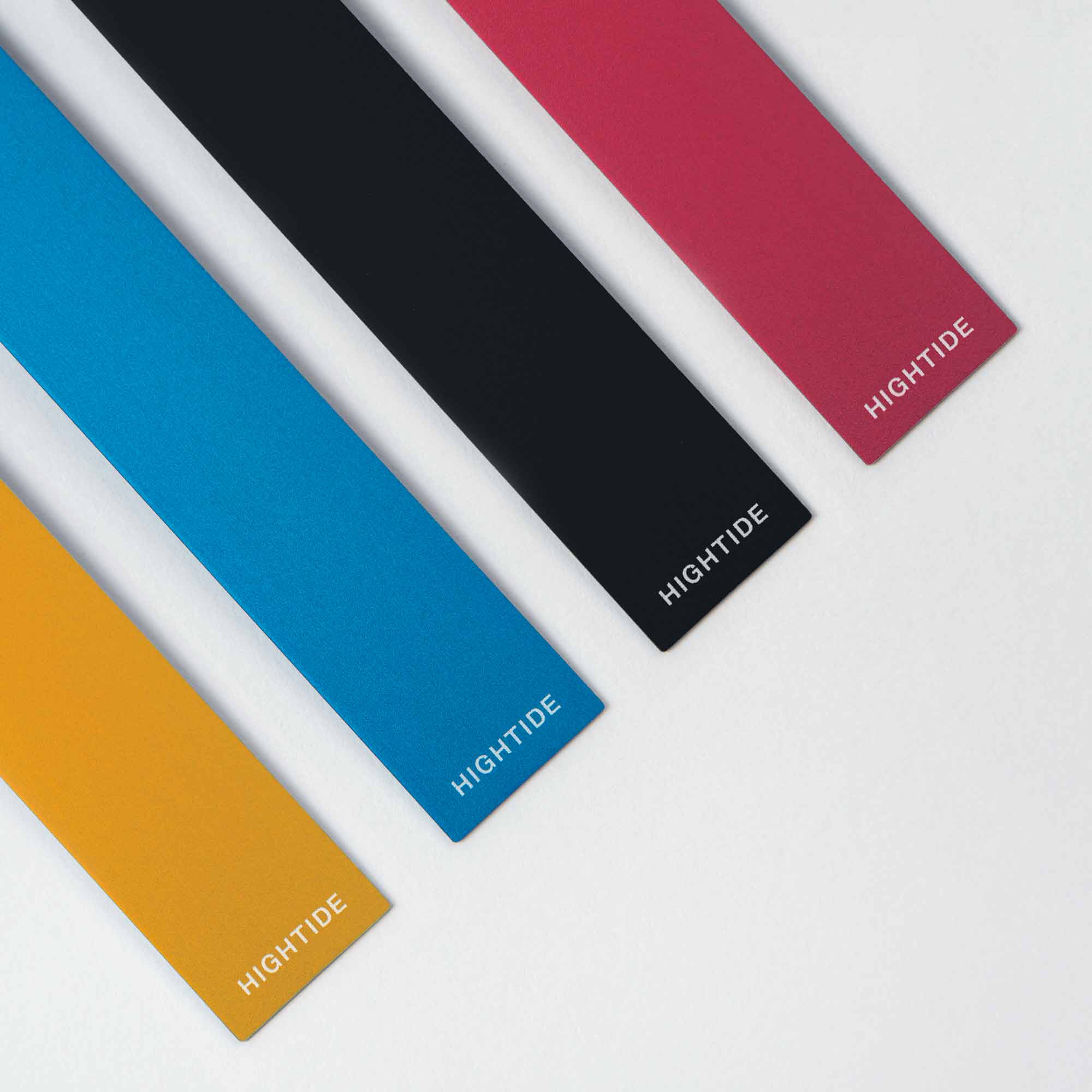Vier rechteckige Clip Rulers, genannt „das Lineal To Go“ von Hightide, sind diagonal auf einer weißen Fläche angeordnet. Die Farben sind Senfgelb, Blau, Schwarz und Pink, an einem Ende ist jeweils der Schriftzug „HIGHTIDE“ in Weiß zu sehen – ideal für dein Bullet Journal oder als Clip Lineal.