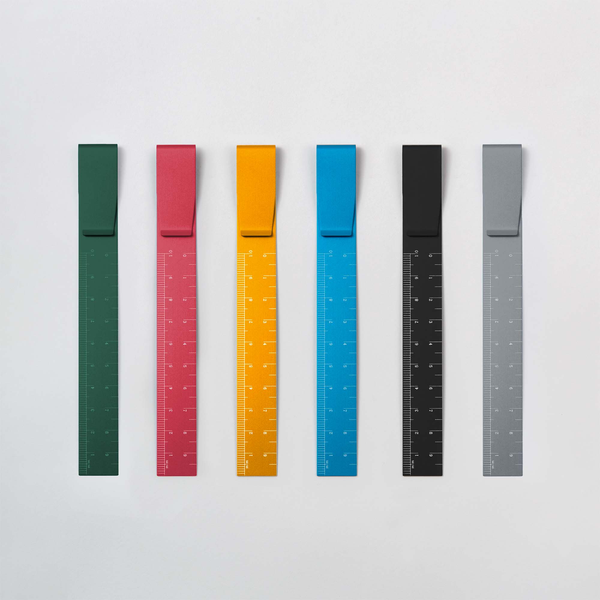 Sechs farbenfrohe Clip Ruler - das Lineal To Go von Hightide sind auf weißem Hintergrund angeordnet. Erhältlich in Grün, Rot, Gelb, Blau, Schwarz und Grau, eignen sich diese Lineale perfekt für präzise Messungen und sind ideal für Bullet Journal-Fans oder Lesezeichen-Sammler.