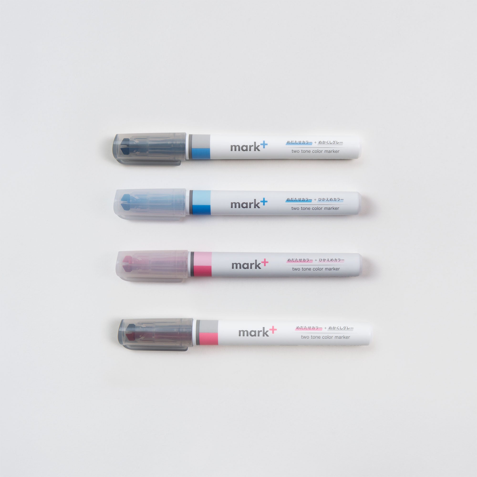 Vier Kokuyo Ein (Text-) Marker, Zwei Farben Stifte mit grauer Kappe sind auf einem weißen Hintergrund aufgereiht. Jeder verfügt über eine blaue, blaue, rosa oder blau/rosa Banderole und das Etikett mark+ zweifarbiger Marker.