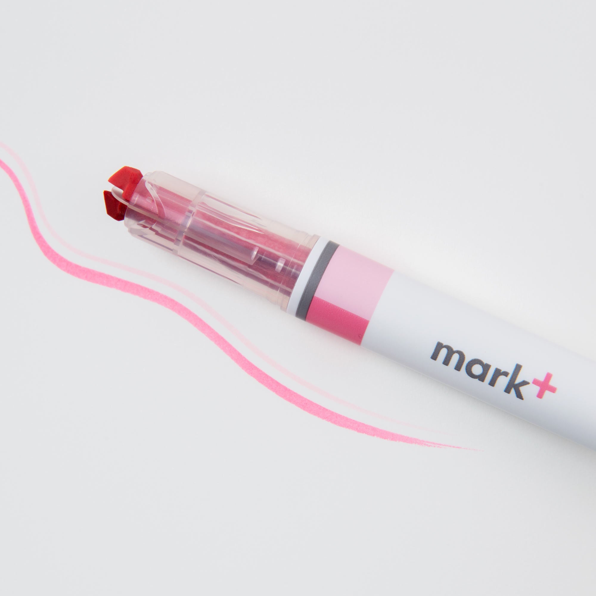 Ein Kokuyo Ein (Text-) Marker, Zwei Farben mit rotem Stift und transparenter Kappe liegt auf einer weißen Oberfläche. Sein rosa-weißer Körper trägt die Aufschrift „mark+“. Eine rosa, gewellte Linie daneben zeigt die leuchtende Farbe und das sanfte Gleiten seiner Fineliner-Spitze für Präzision.