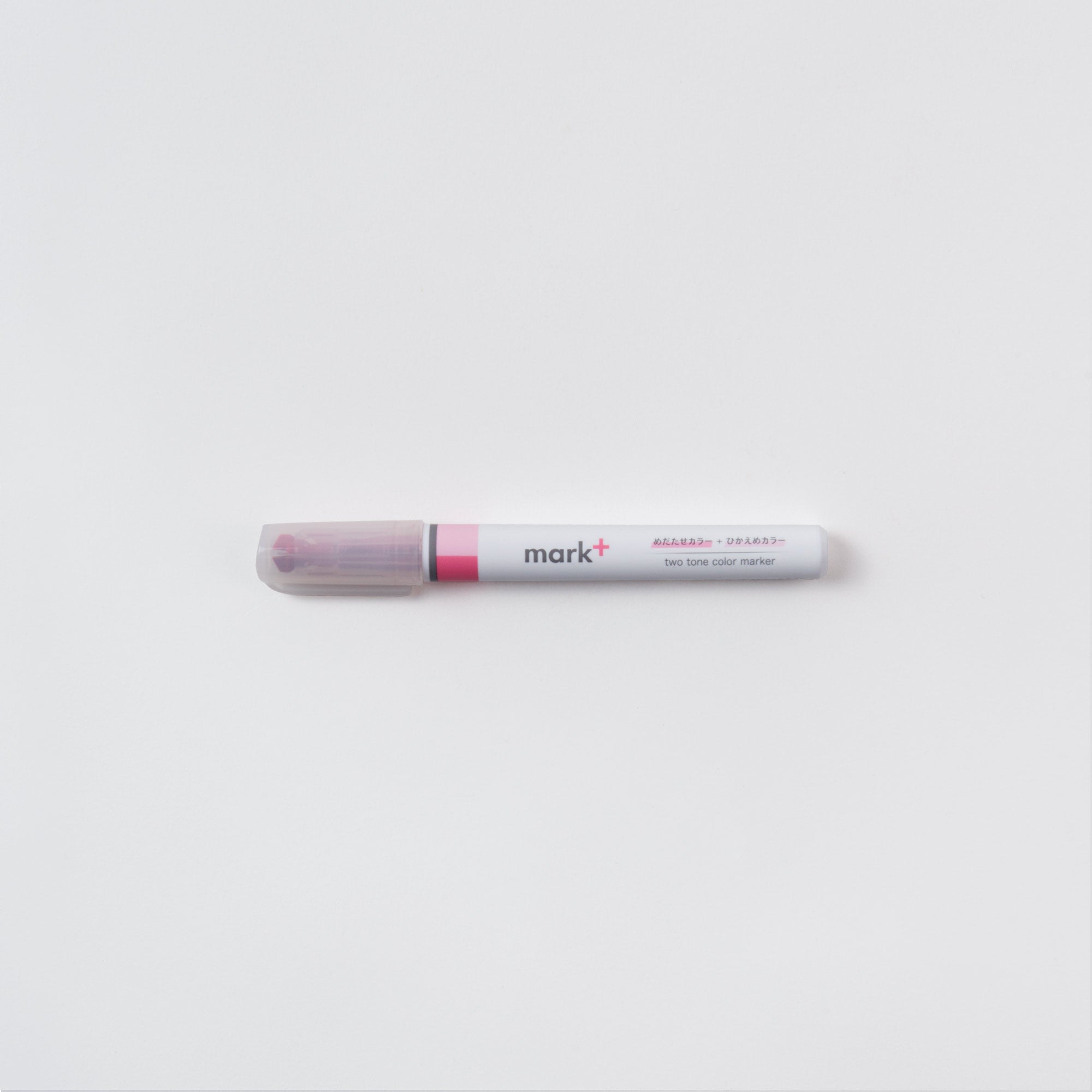 Ein doppelseitiger Kokuyo-Stift mit der Aufschrift „Ein (Text-) Marker, Zwei Farben“ und grauer Kappe liegt auf einer weißen Oberfläche. Er ist für doppelte Markierungen gedacht, ein Ende ist leicht erhöht und wirft einen Schatten.