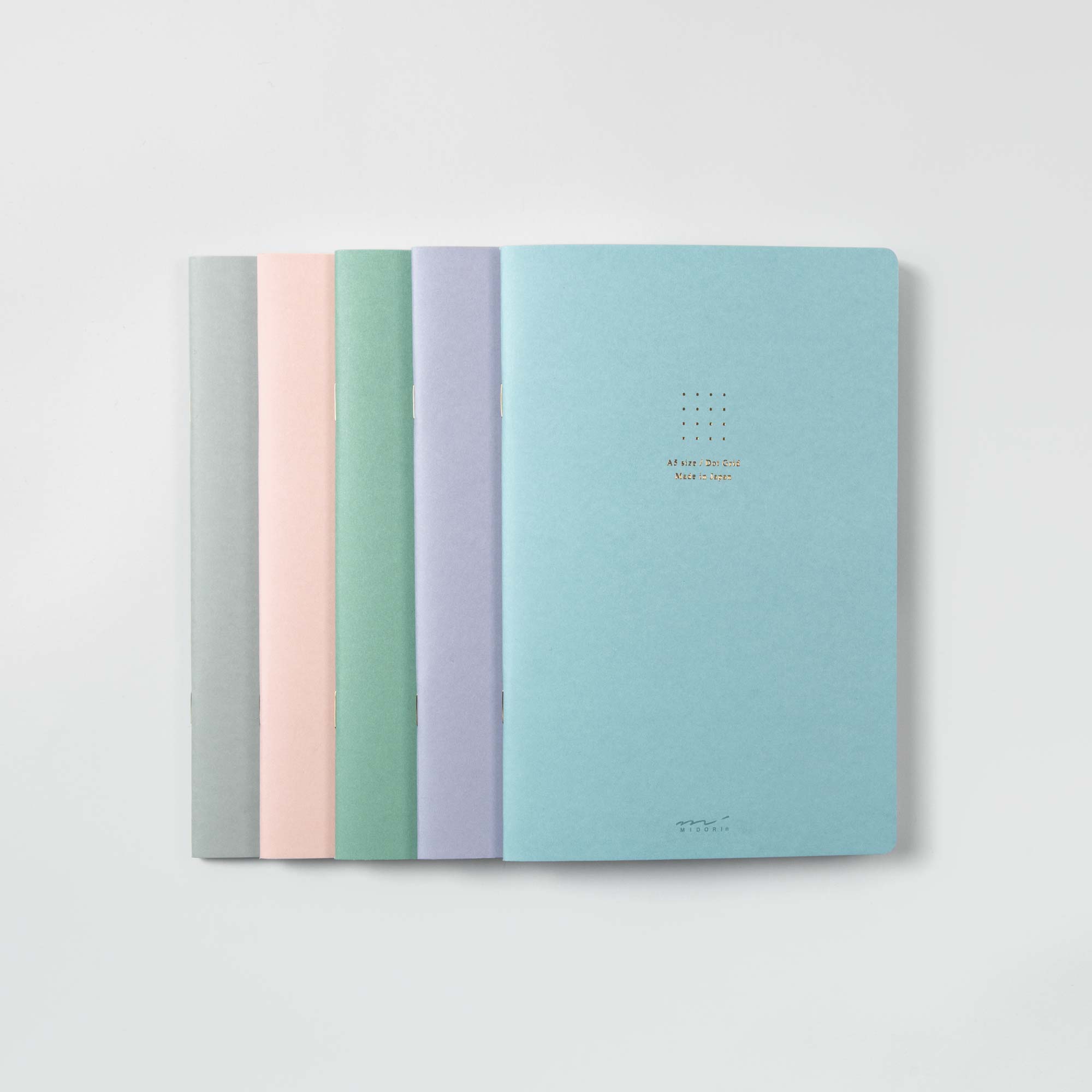 Fünf schmale Notizbücher Midori Notizhefte Color Dot Grid sind in beruhigenden Pastelltönen erhältlich: Grau, Rosa, Grün, Blau und Blaugrün. Jedes hat ein minimalistisches Design mit dezentem Covertext und steht vor einem schlichten weißen Hintergrund.