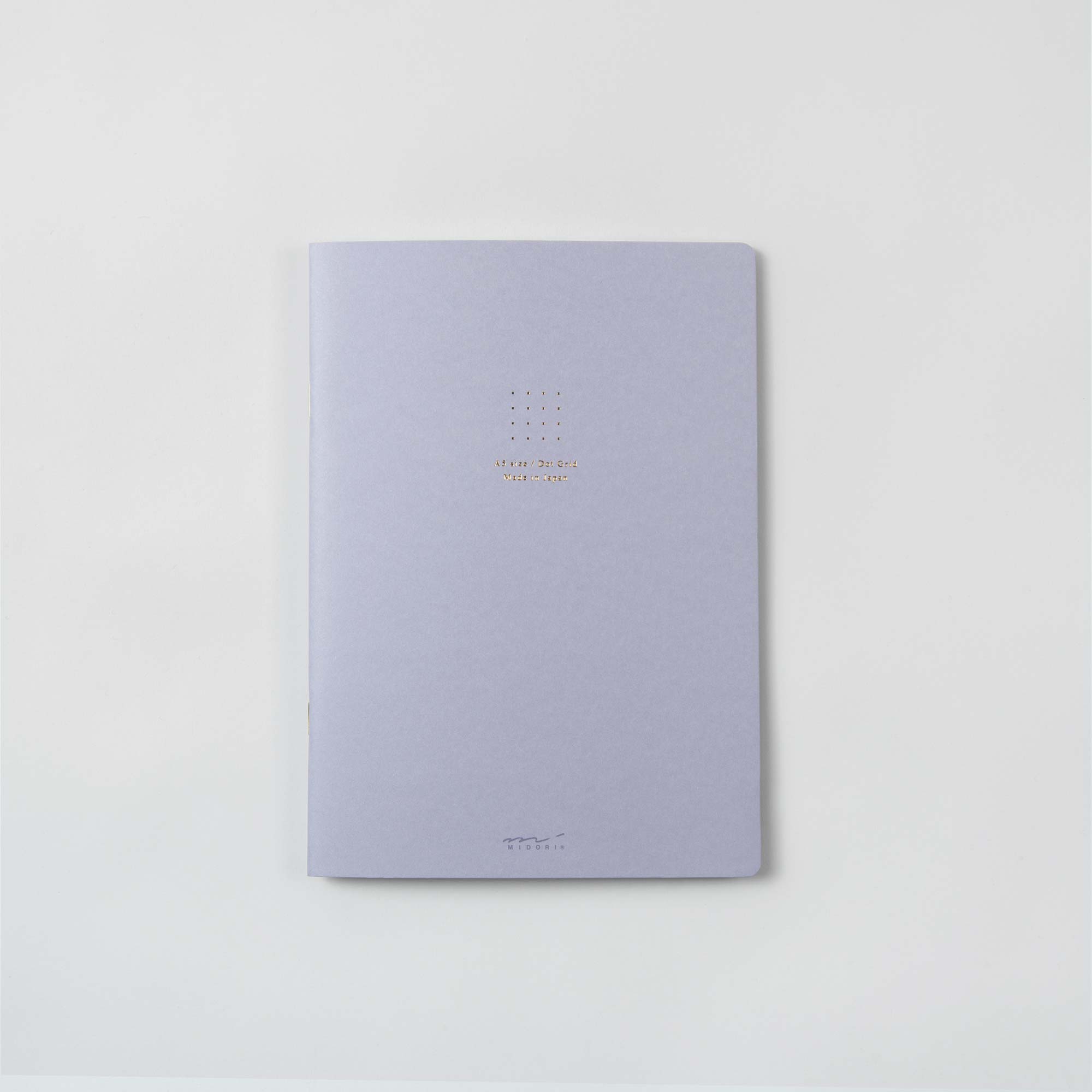 Ein sanftes graublaues „Notizhefte Color Dot Grid“ von Midori liegt auf einer weißen Oberfläche. Der Einband zeigt ein einfaches heißfoliengeprägtes Goldpunktdesign über fettem Text, mit minimalistischem Branding am unteren Rand, das elegante Pastelltöne verkörpert.