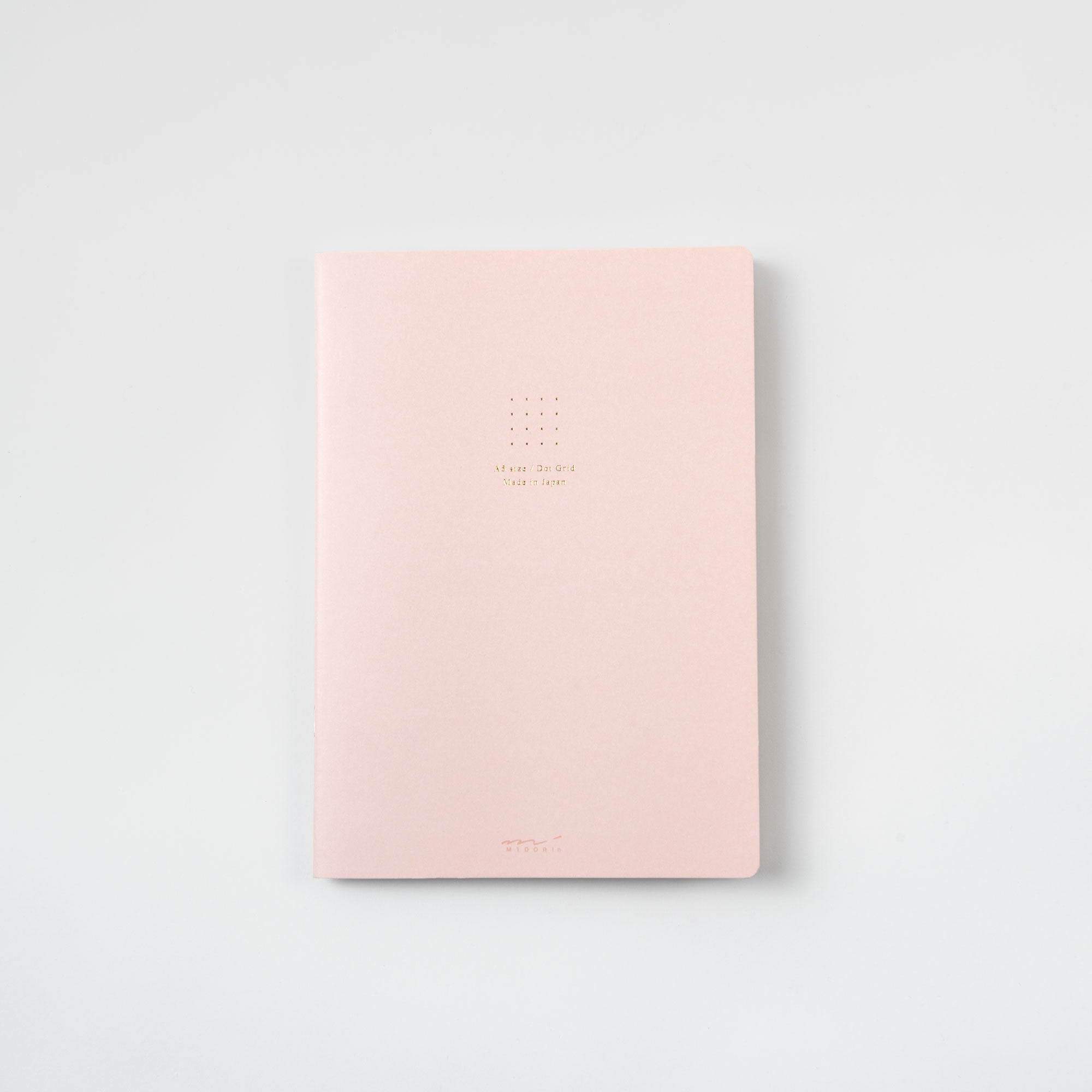 Ein pastellrosa Notizbuch vom Typ „Midori Notizhefte Color Dot Grid“ liegt auf einer weißen Oberfläche, sein minimalistischer Einband mit einem gepunkteten Raster und kleinem Text in der Mitte bietet eine subtile dekorative Note.