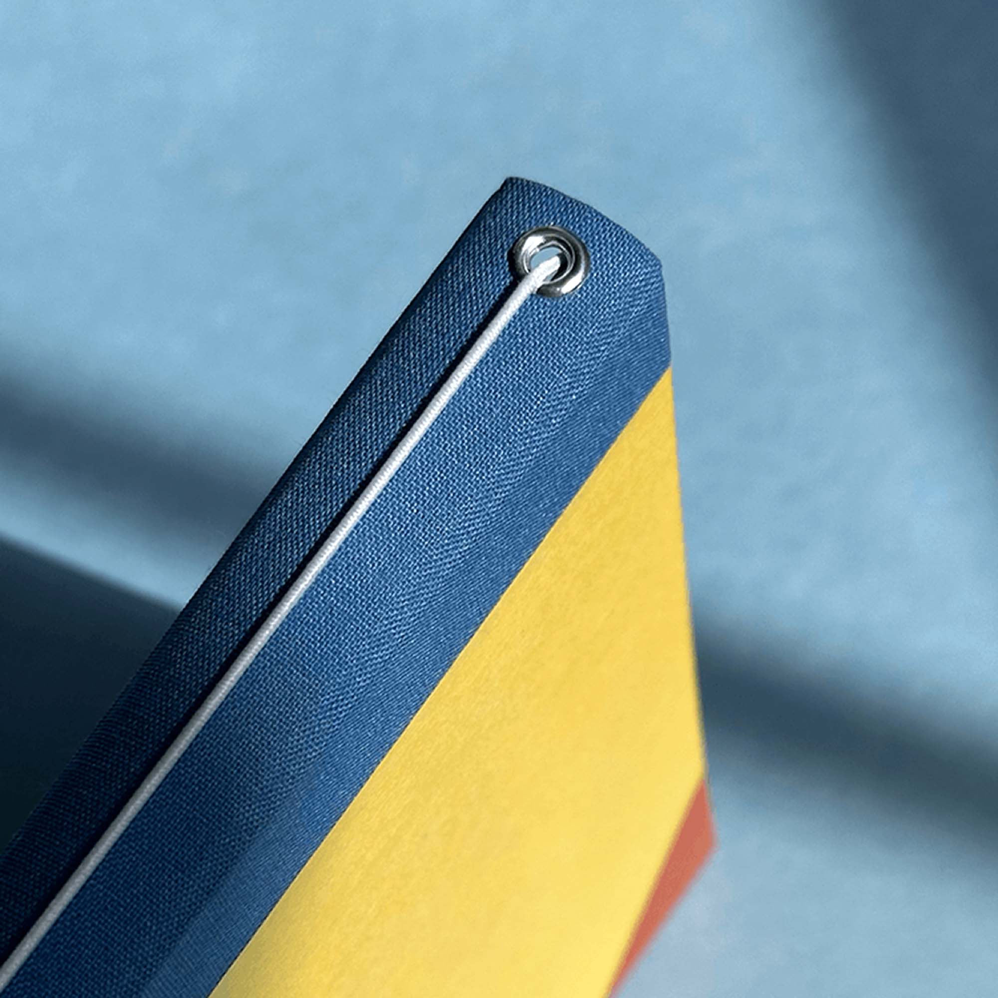 Nahaufnahme eines gebundenen Modularen Notizbuchs von paperlux.store mit blauem Buchrücken, gelbem Einband, rotem Detail und weißer Gummikordel durch eine Metalltülle - die ideale Inspiration für Ihren Workshop Modulares Notizbuch.