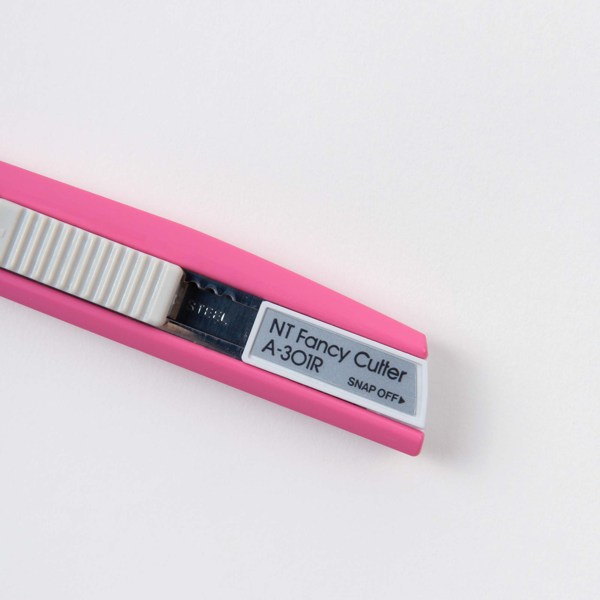 Nahaufnahme eines rosa NT Cutter Universalmessers mit weißem einziehbarem Klingenschieber, ideal für präzises Schneiden und Basteln. Auf der metallischen Klingenabdeckung steht „NT Fancy Cutter A-30IR SNAP OFF“. Sie ruht elegant auf einer weißen Oberfläche.