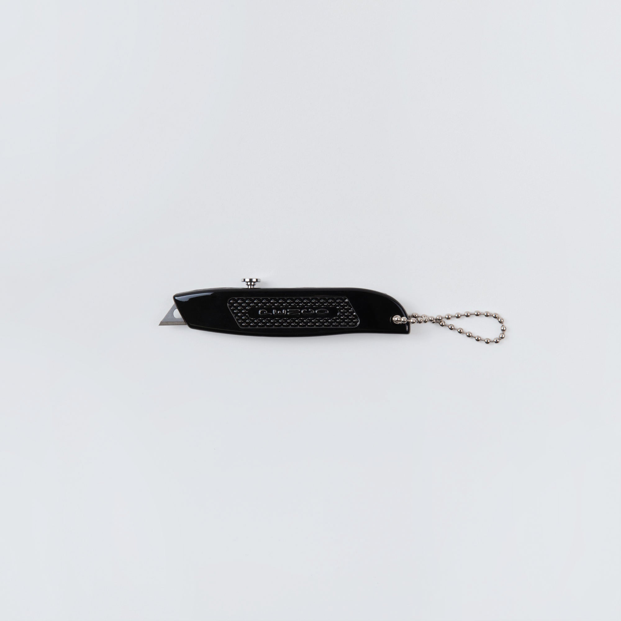 Das Penco Allzweckmesser - auch bekannt als der Cutter an der Kette - in Schwarz mit kleiner, ausgefahrener Klinge und silberner Kugelkette liegt auf schlicht weißem Hintergrund, ideal zum Öffnen von Paketen.
