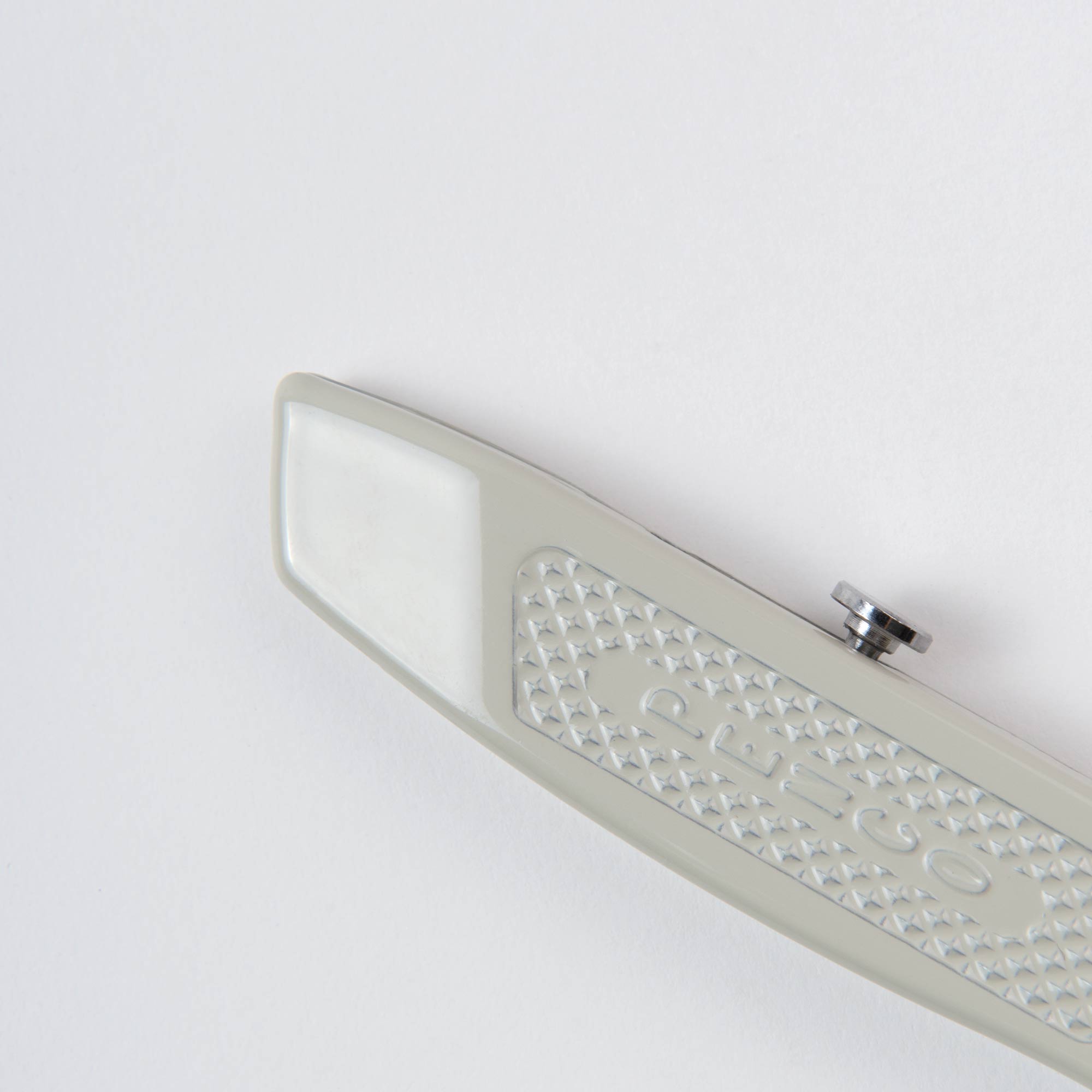 Eine Nahaufnahme eines grauen Penco Allzweckmessers - oder auch: der Cutter an der Kette mit strukturiertem Griff auf einer weißen Oberfläche. Das minimalistische Design zeigt einen Teil der Klinge und ein kleines rundes Metallteil oben drauf und betont so seinen funktionalen Reiz.