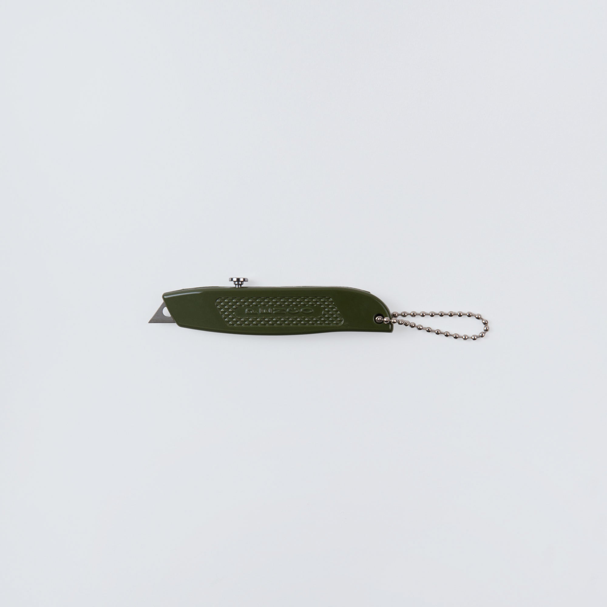 Das Allzweckmesser - oder auch: der Cutter an der Kette von Penco ist ein grünes Messer mit kleiner, teilweise sichtbarer Klinge und Metallkette, perfekt zum Pakete öffnen, abgebildet auf weißem Hintergrund.