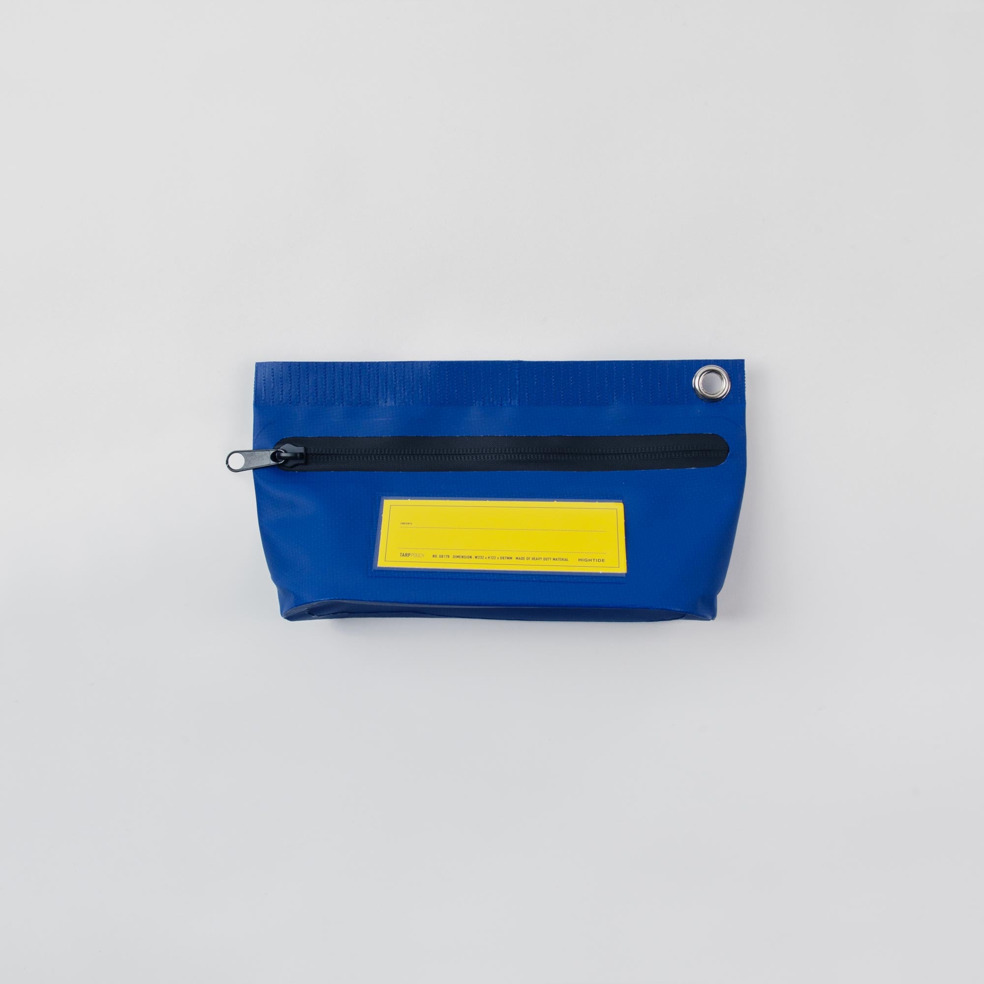 Die Tarp Pouch S von Penco ist eine kleine blaue Tasche aus Planenmaterial, mit schwarzem Reißverschluss, silberner Öse auf einer Seite und leuchtend gelbem Frontlabel. Der Hintergrund ist hellgrau.