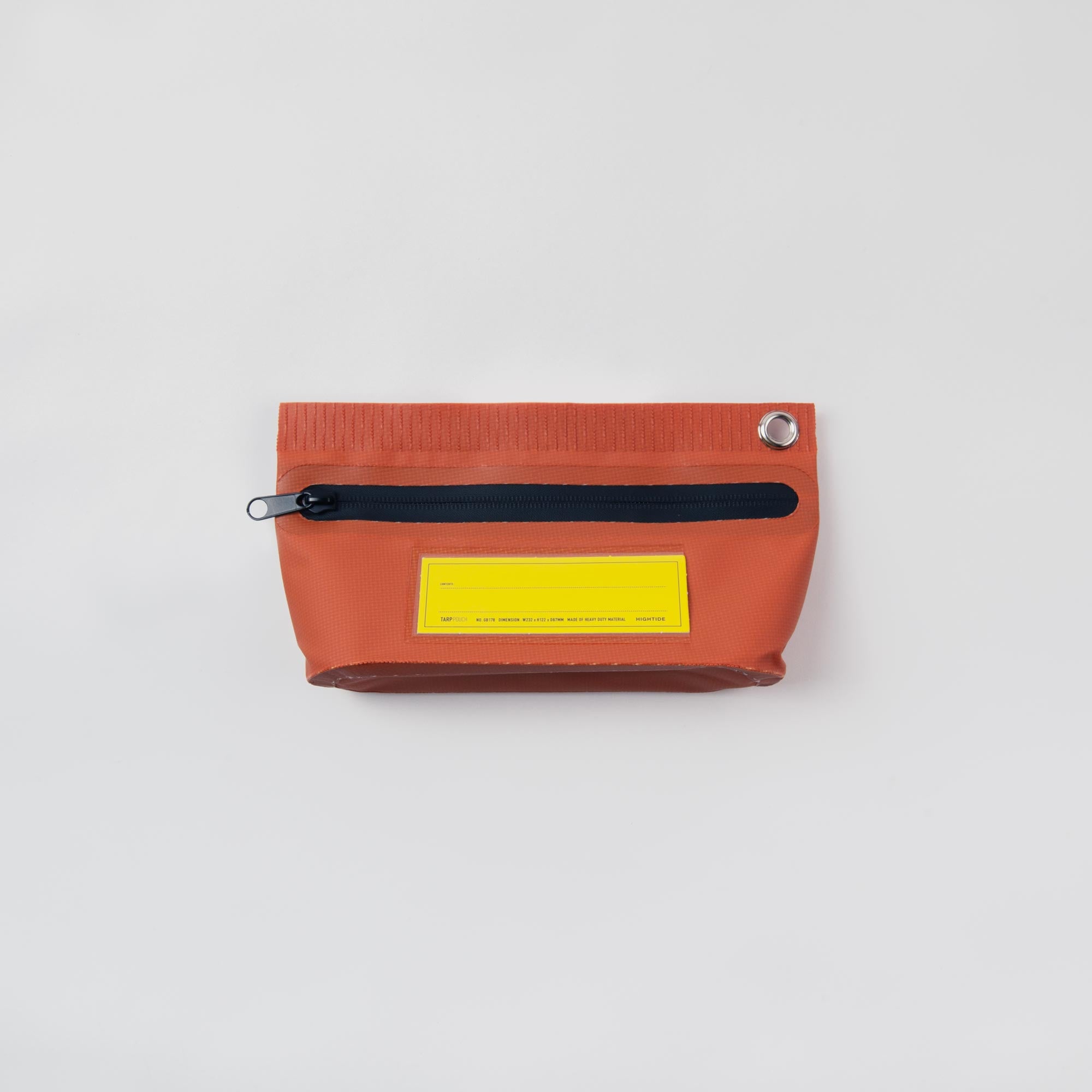 Die Penco Tarp Pouch S ist eine kleine rote Tasche aus Planenmaterial mit einem schwarzen Reißverschluss mit wasserdichten Verschlüssen, einem Metallring in der oberen rechten Ecke und einem gelben rechteckigen Etikett unter dem Reißverschluss vor einem schlichten weißen Hintergrund.