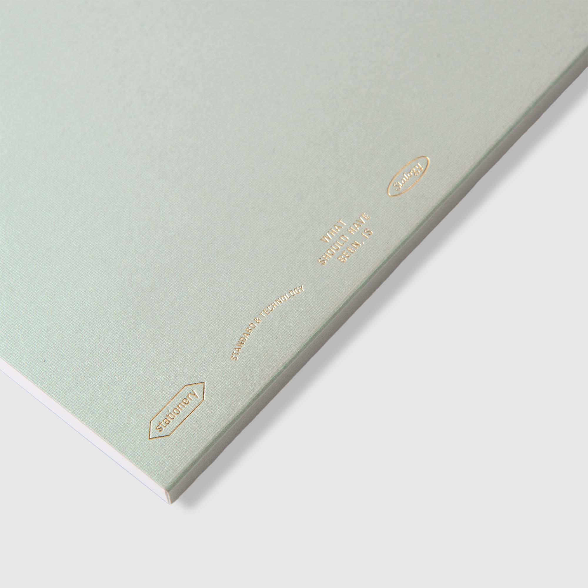 Das Stalogy Editor's Series 1/2 Year Notebook A5 Limited Edition zeichnet sich durch einen minimalistischen hellgrauen Einband mit goldgeprägtem Text und einem Perlglanzeffekt sowie kleinen ovalen Etiketten in der Ecke auf weißem Hintergrund aus.