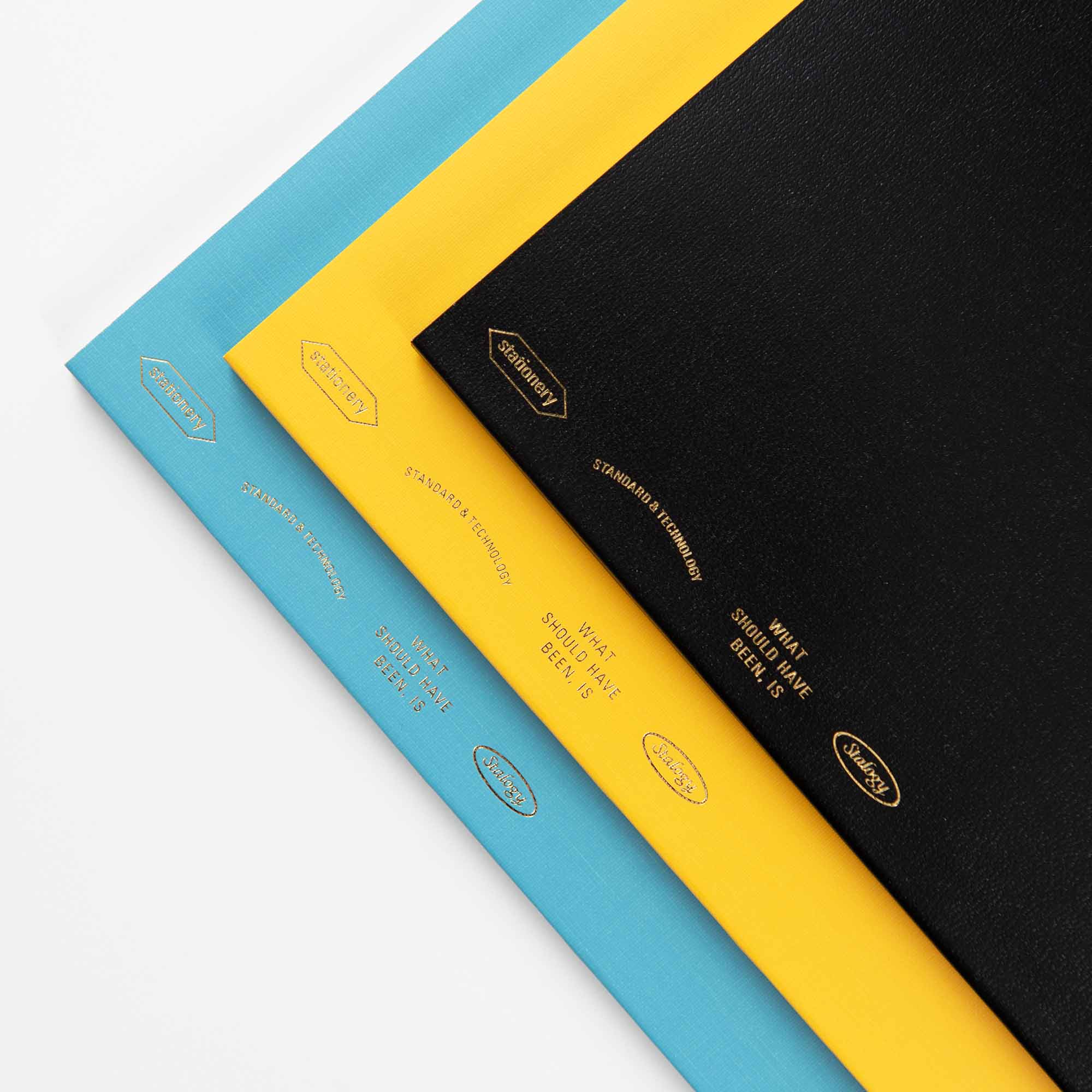 Drei übereinanderliegende Notizbücher – eines blau, eines gelb und eines schwarz – aus der Stalogy Editors Series 1/2 Year Notebook B6. Sie verfügen über goldgeprägte Texte und Logos auf dem Einband. Das B6-Format bietet hervorragende Möglichkeiten zur individuellen Gestaltung.