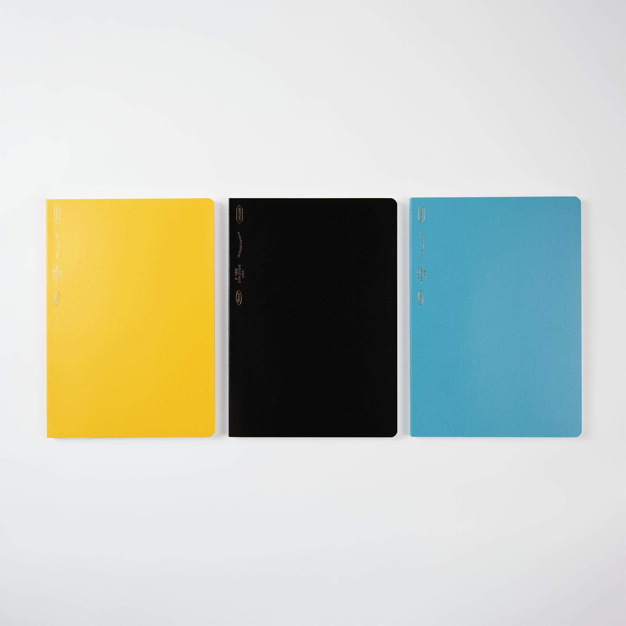 Drei geschlossene Notizbücher auf weißem Hintergrund: links gelb, in der Mitte schwarz und rechts blau. Sie sind Teil von Stalogys Editors Series 1/2 Year Notebook B6 und zeichnen sich durch minimalistisches Design mit subtilen grafischen Elementen auf den Umschlägen aus.