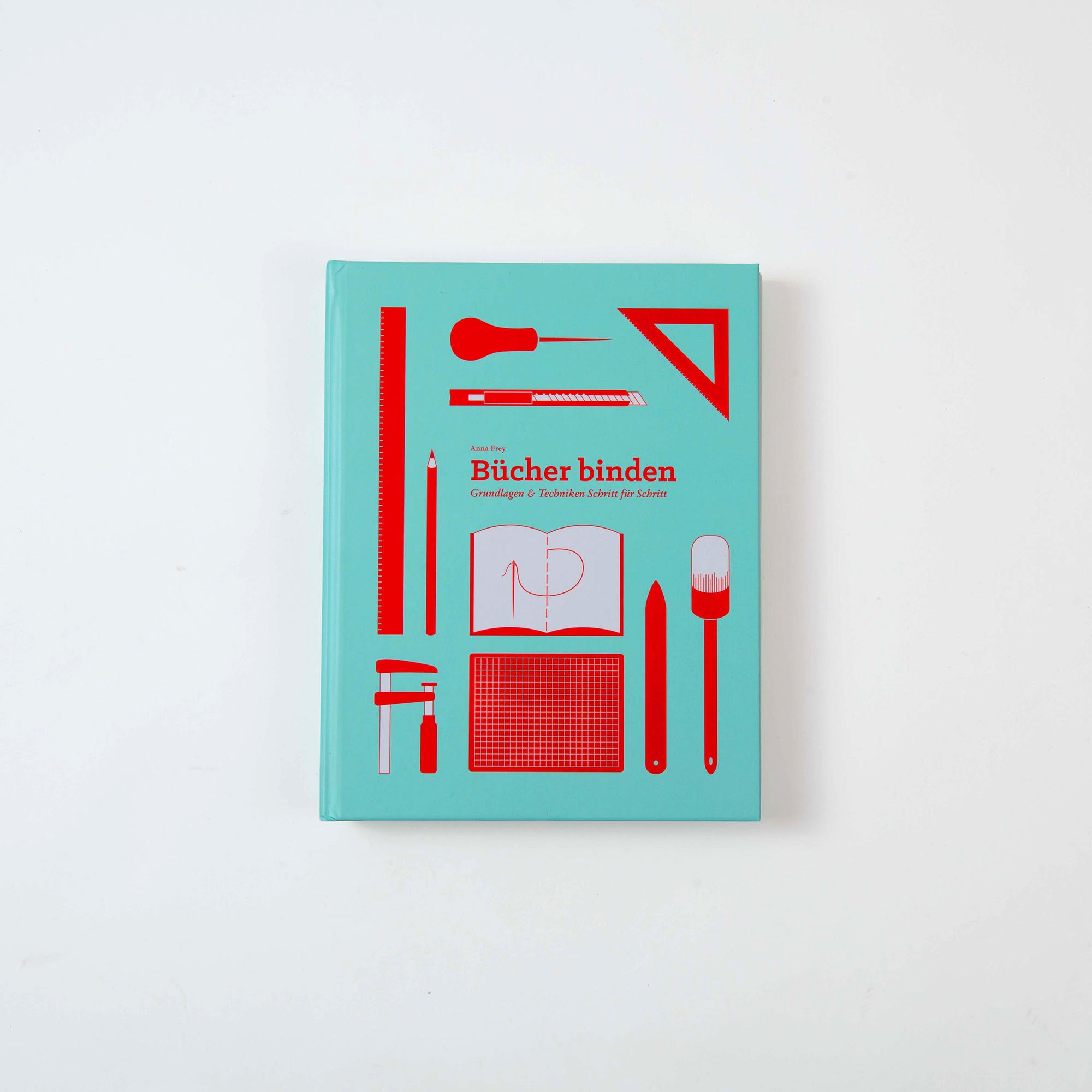 Bücher binden" von Anna Frey, ein blaugrünes Buch mit roten Abbildungen von Buchbindewerkzeugen und Diagrammen auf dem Einband, wird auf einem schlichten weißen Hintergrund präsentiert.
