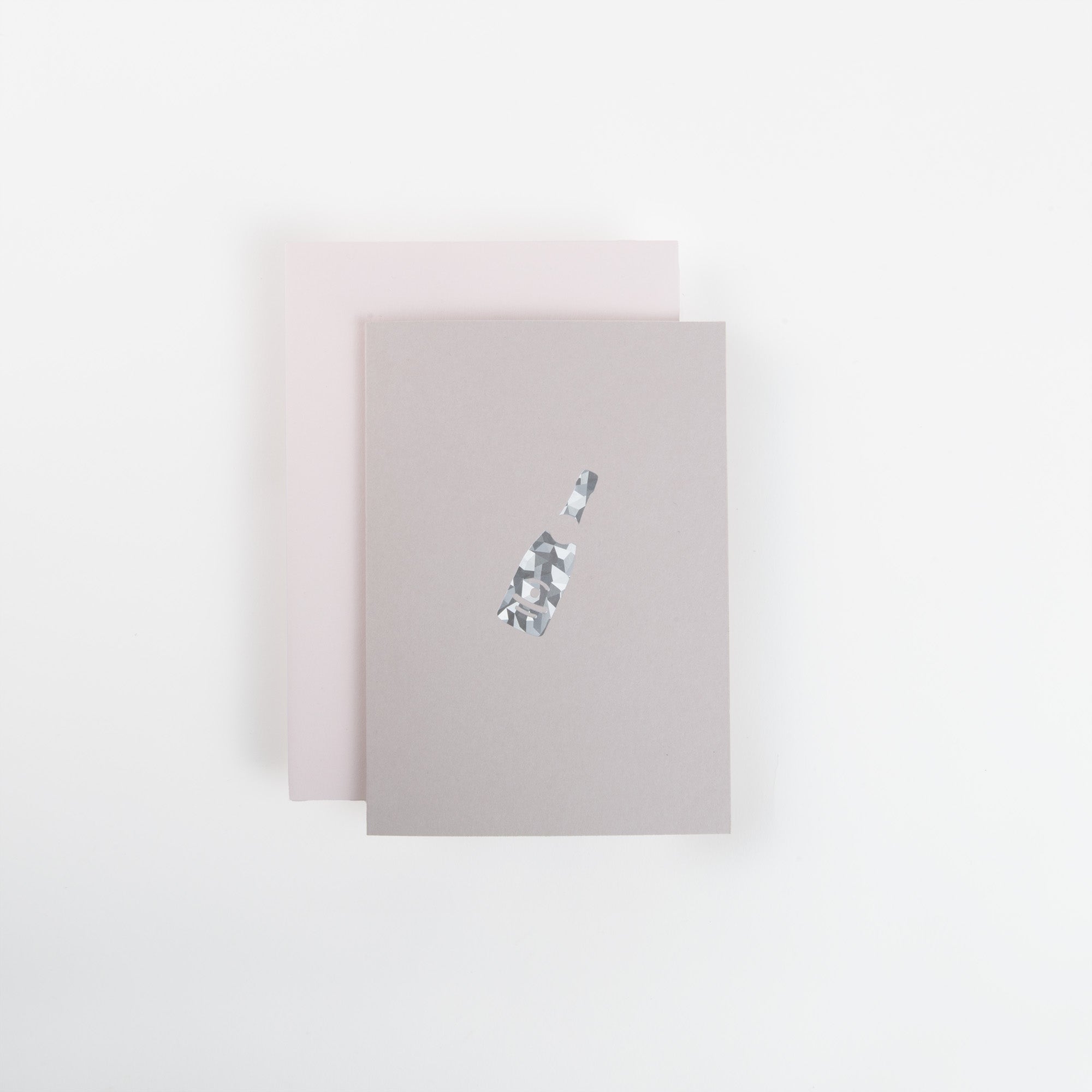 Auf einer weißen Fläche überlagern sich zwei minimalistische Notizbücher von paperlux.store: oben die A6-Karte "Champagner" mit einem kleinen, abstrakten Flaschendesign, darunter ein blassrosa Notizbuch.