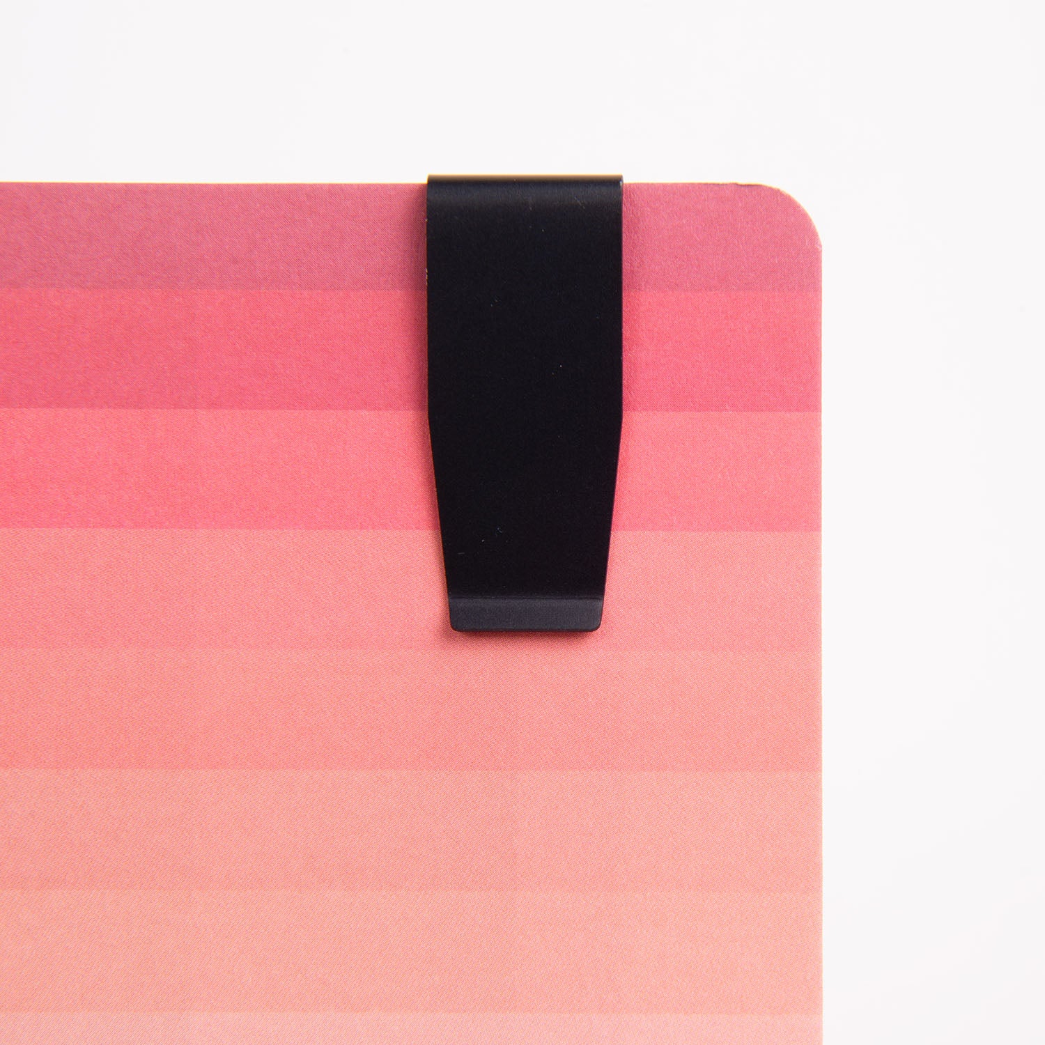 Ein Clip-Lineal – das Lineal To Go von Hightide sichert einen Stapel rosa Papier mit Farbverlauf und von hell nach dunkel übergehenden Farbtönen, perfekt für ein Bullet Journal, vor einem schlichten weißen Hintergrund, der seine Eleganz unterstreicht.