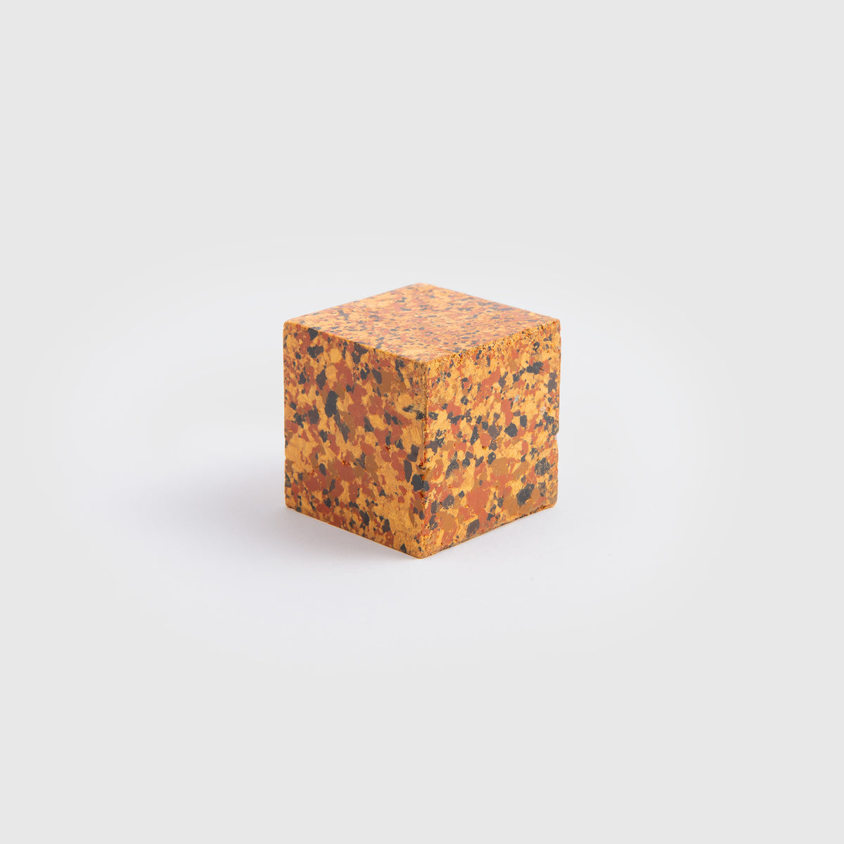 Ein kleiner Würfel aus der „Color Gem“-Reihe von Studio Unto – das Wachsmalquadrat – Einzelpackung, der auf allen Seiten ein gesprenkeltes Muster aus Orange, Gelb und Schwarz aufweist und von „Zeichnen aus der Natur“ inspiriert ist, wird vor einem schlichten weißen Hintergrund präsentiert.