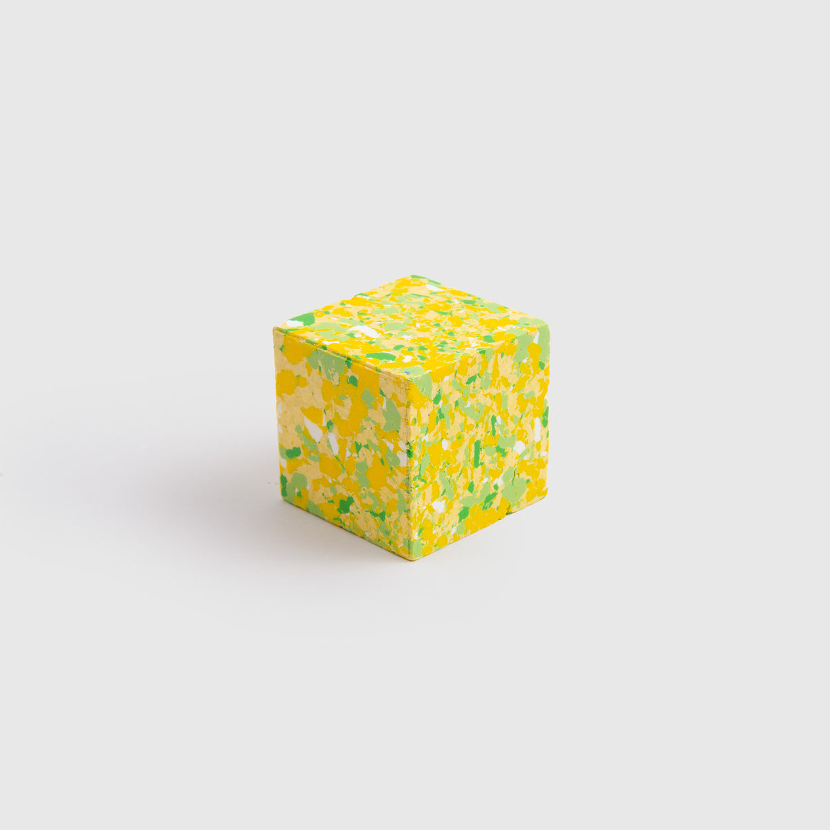 Ein kleiner Würfel von Studio Unto, der „Color Gem – das Wachsmalquadrat“ Einzelpackung, mit einem gesprenkelten Muster aus Gelb, Grün und Weiß, liegt auf einem schlichten weißen Hintergrund und ist von „Zeichnen aus der Natur“ inspiriert.