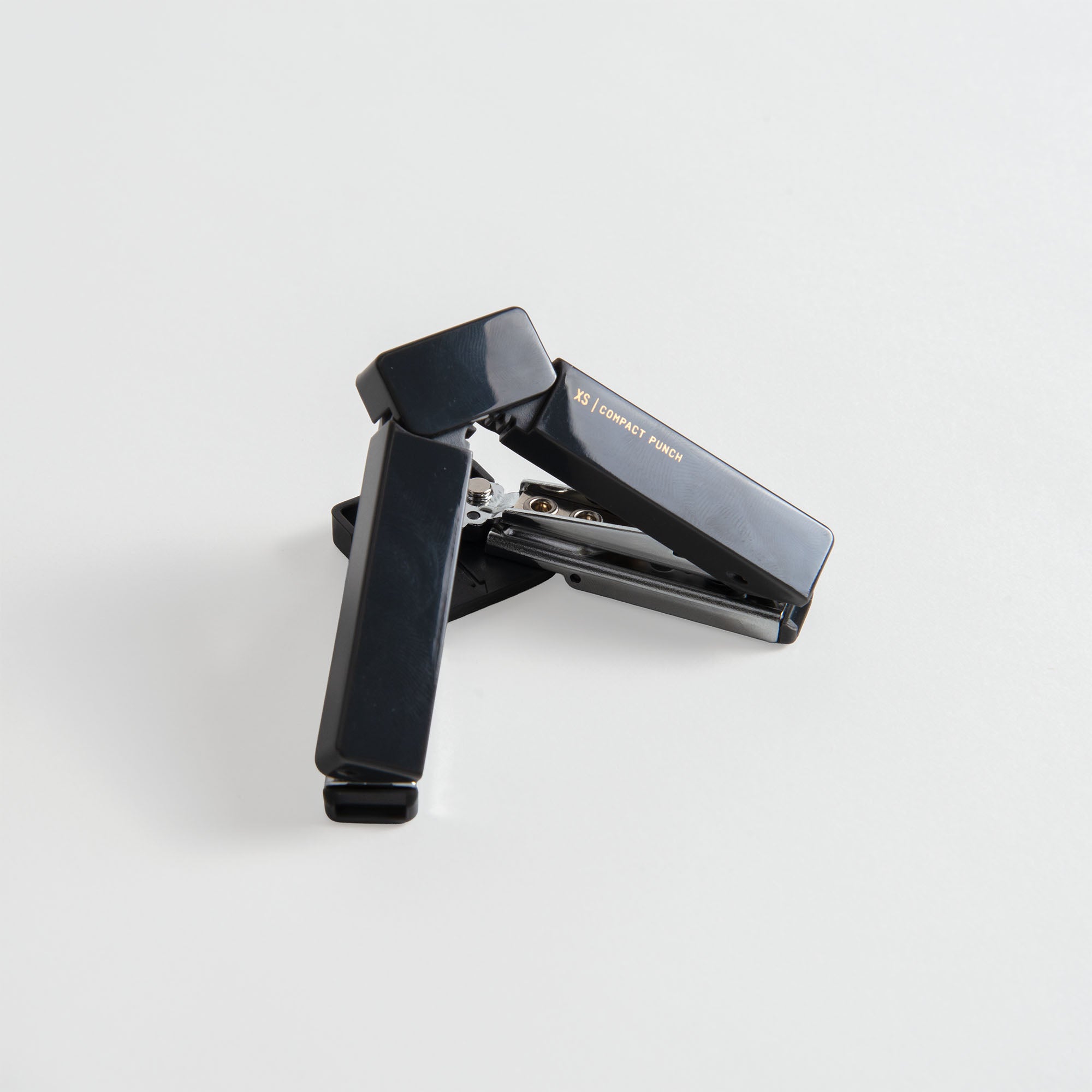 Ein schwarzer Hefter liegt offen auf einer weißen Fläche, sein Metallmechanismus ist sichtbar, daneben steht der Midori XS Compact Punch von Midori-ein kompakter Locher für den mobilen Einsatz.