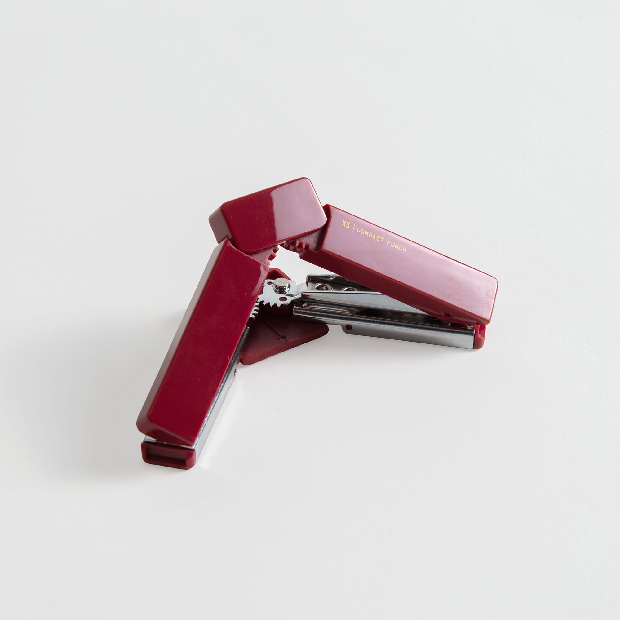 Ein kastanienbrauner Hefter liegt offen auf einer weißen Fläche neben dem Midori XS Compact Punch von Midori, einem idealen tragbaren Werkzeug für die Organisation von Dokumenten unterwegs.