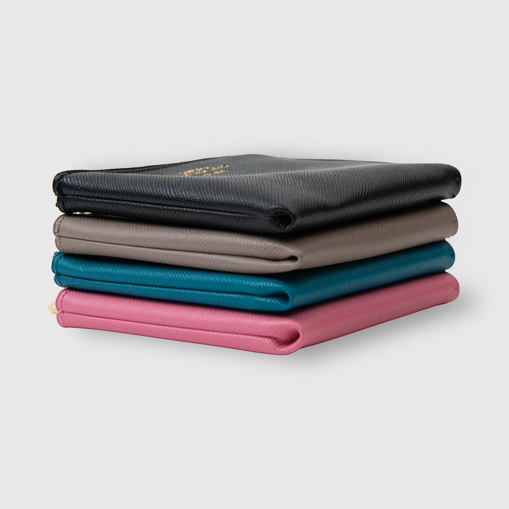 Ein Stapel aus vier „Delfonics Quitterie Half Zip Card Case | Kartenetui“-Geldbörsen in Schwarz, Grau, Blau und Rosa – jede mit einem eleganten Design im Scotch-Grain-Look von Delfonics – ist ordentlich auf einem hellgrauen Hintergrund angeordnet.