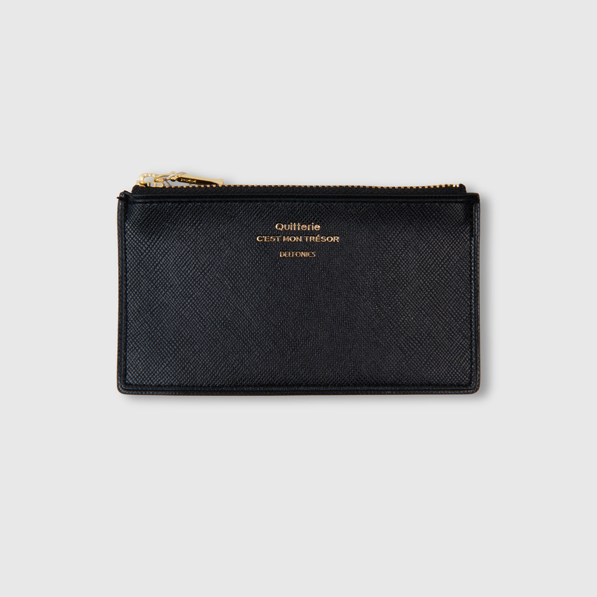 Eine schwarze, strukturierte Geldbörse mit Reißverschluss, deren offizielle Bezeichnung „Delfonics Quitterie Card Zip Case“ lautet, besticht durch eine elegante goldene Aufschrift auf der Vorderseite mit dem Text „Quitterie Cest Mon Trésor DELFONICS“, die sich von einem schlichten hellgrauen Hintergrund abhebt.