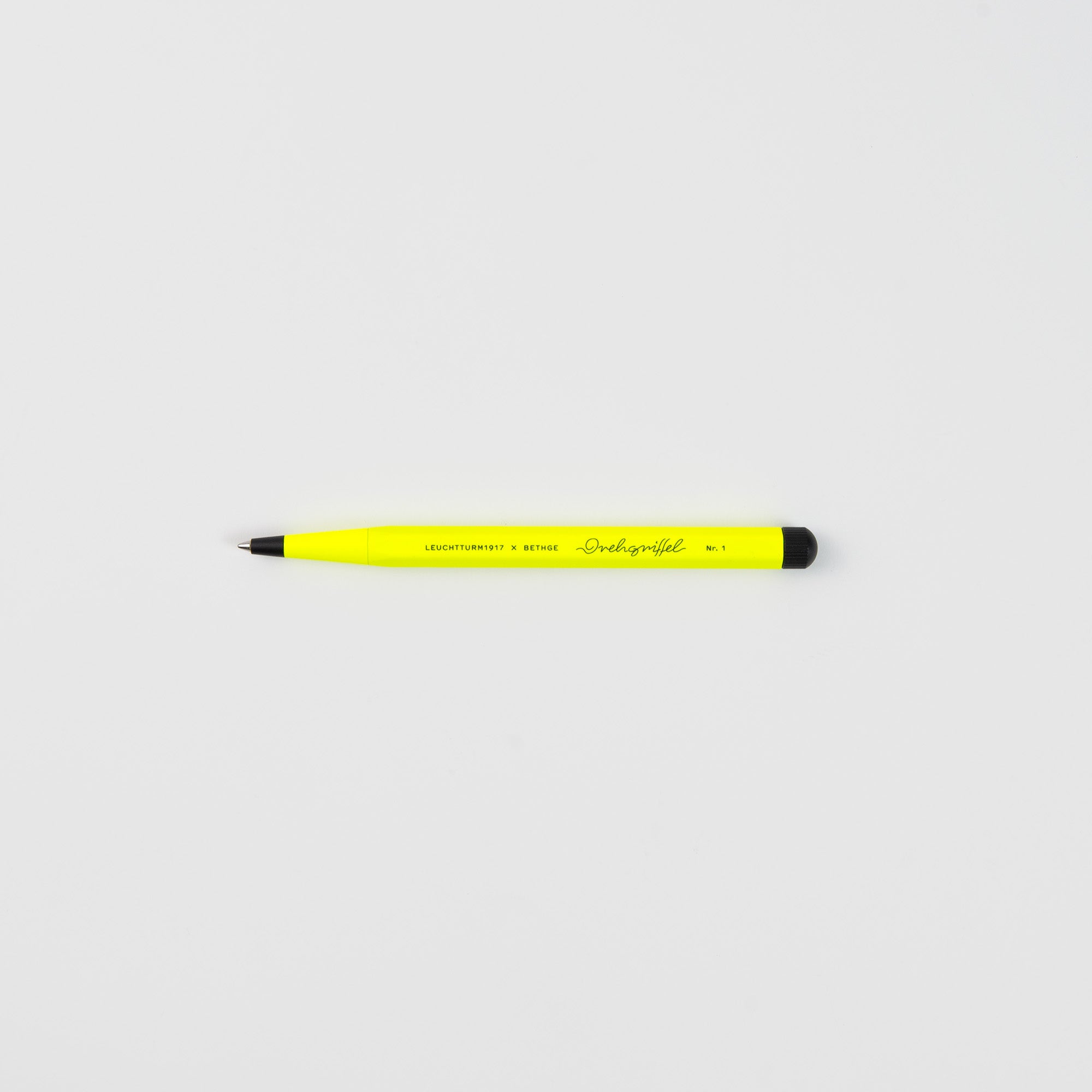 Ein gelber Leuchtturm 1917 Drehgriffel No. 1 Luminous Edition Kugelschreiber mit schwarzer Spitze und Endkappe ruht waagerecht auf einer schlichten weißen Fläche, auf der seitlich ein Text aufgedruckt ist.