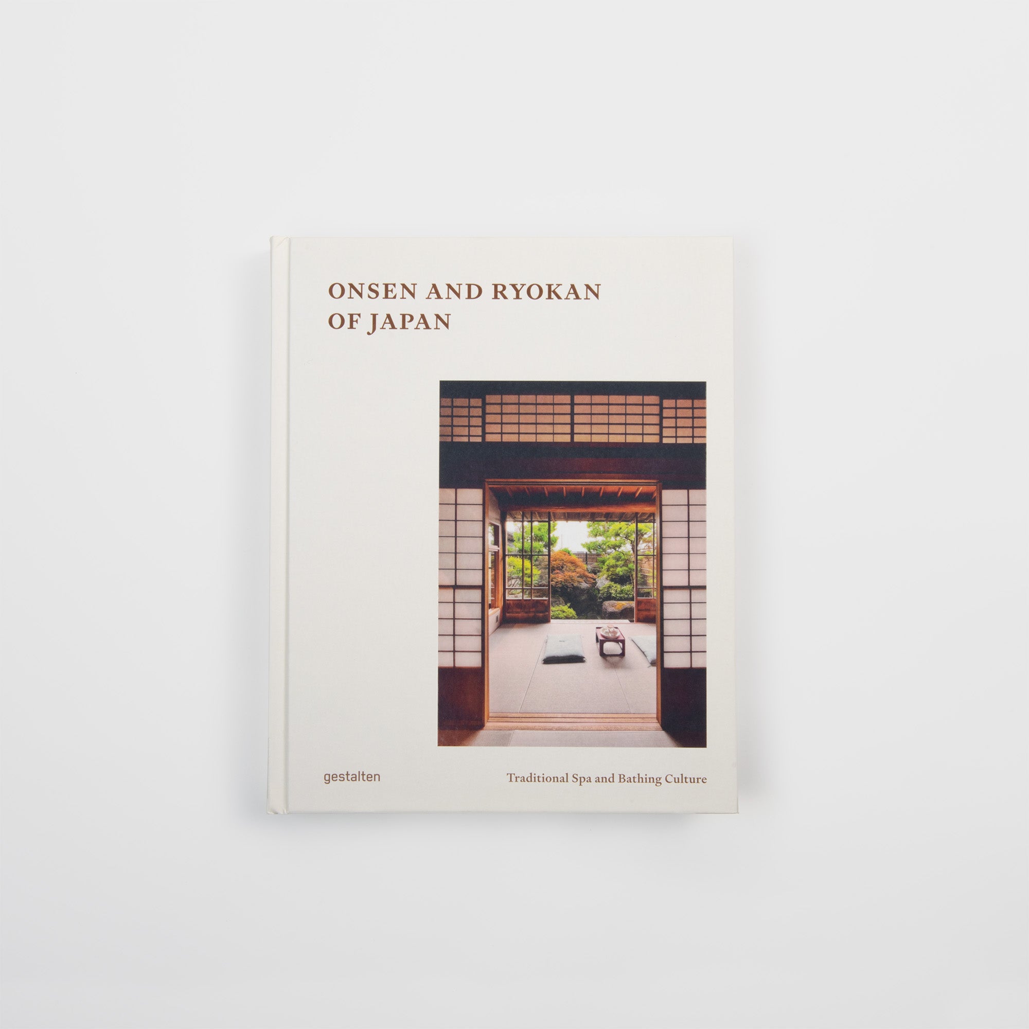 Das Buch "Onsen & Ryokan of Japan - Ein Blick in Japans stille Welten" aus dem Gestalten Verlag zeigt auf dem Cover ein traditionelles japanisches Zimmer mit offenen Schiebetüren und einem Garten, das Onsen Japan und authentische Gastfreundschaft auf einem schlichten weißen Hintergrund verkörpert.