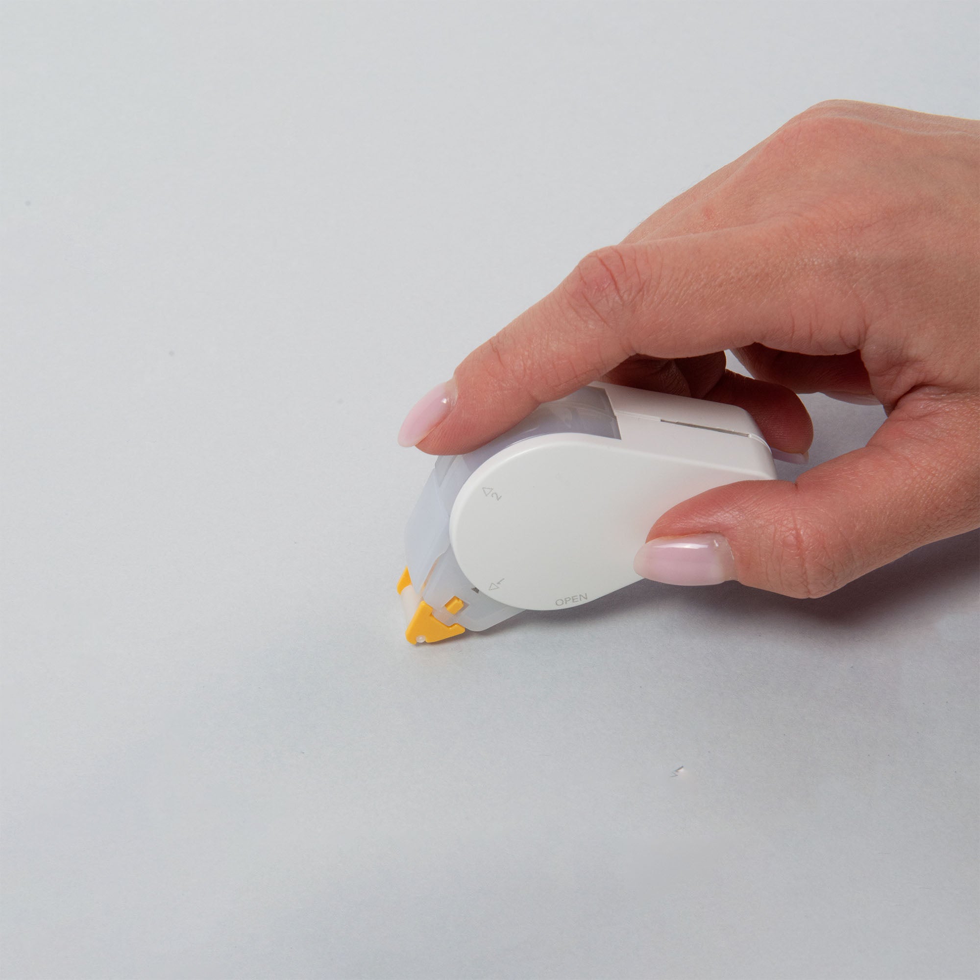 Eine manikürte Hand verwendet einen glatten, repositionierbaren Kokuyo GLOO Tape Klebestreifen auf einer weißen Oberfläche und kaschiert mit seinem weißen Design und den gelben Akzenten mühelos Fehler, was den Benutzer sofort fasziniert.