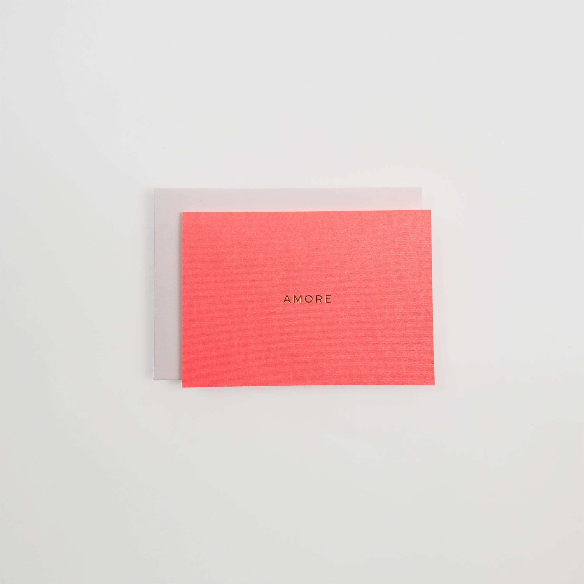 Ein Kärtchen AMORE von Gmund in Rot mit goldenem Schriftzug sitzt auf einem hellgrauen Gmund-Briefumschlag, der auf einem schlichten weißen Hintergrund steht.