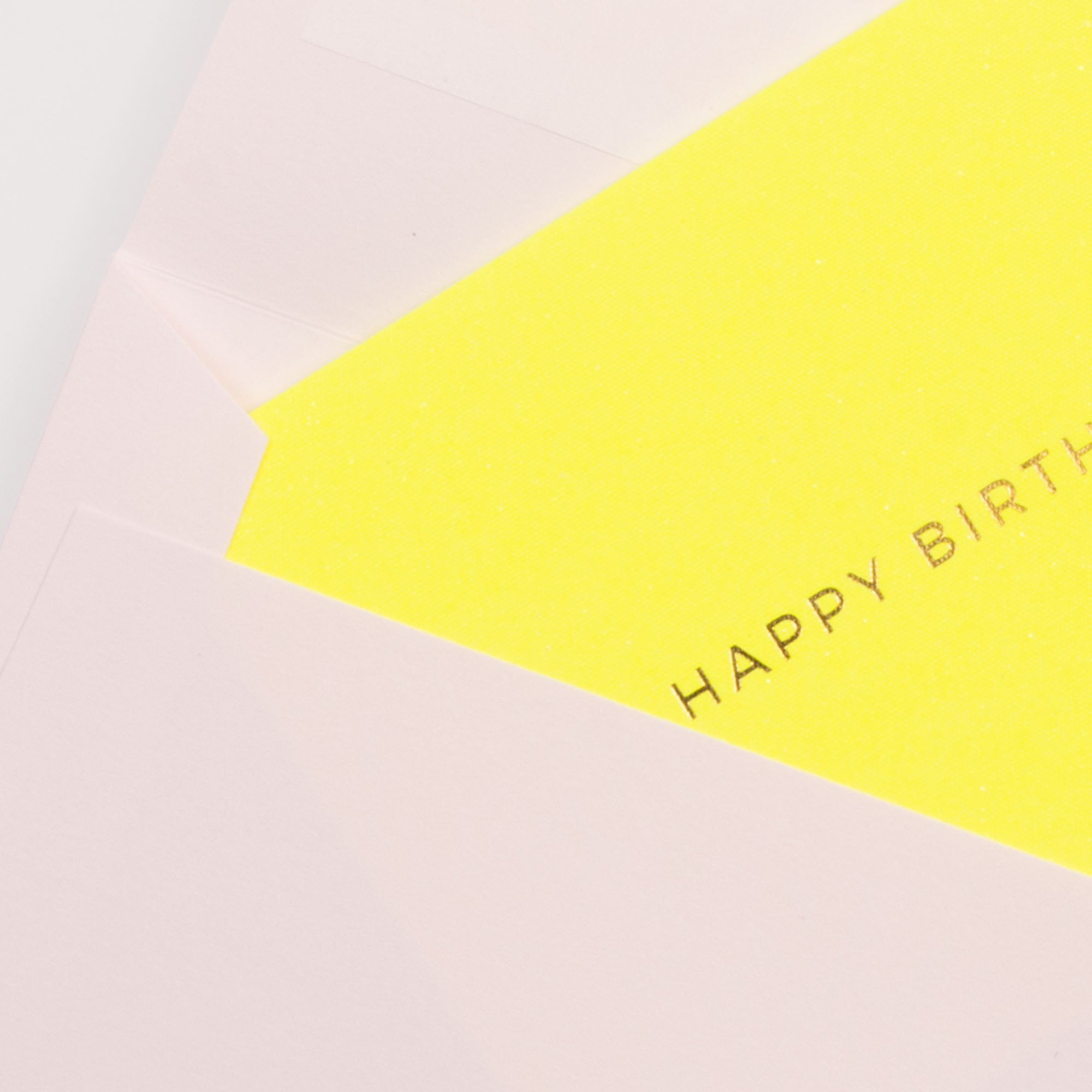Die Letterpress-Karte Kärtchen HAPPY BIRTHDAY von Gmund, in leuchtendem Gelb mit partiellem HAPPY BIRTH-Text, lugt aus einem hellrosa Gmund Little Color Notes-Umschlag auf weißem Hintergrund hervor.
