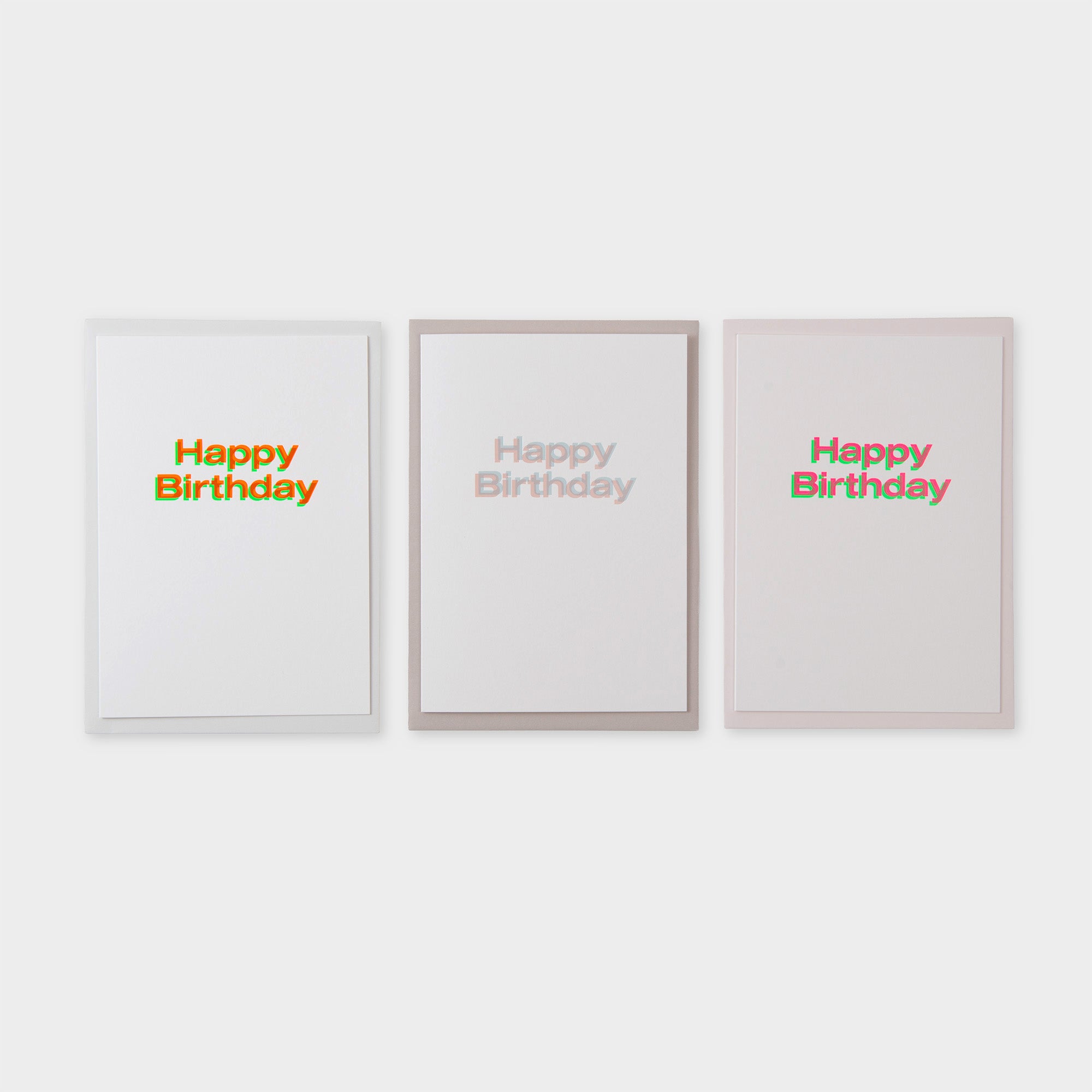 Drei Happy Birthday Karten A5 von paperlux.store sind nebeneinander auf weißem Hintergrund abgebildet; die erste und dritte Karte haben einen fetten, bunten Text, während die mittlere Karte einen schwachen grauen Text zeigt. Hergestellt in Hamburg.