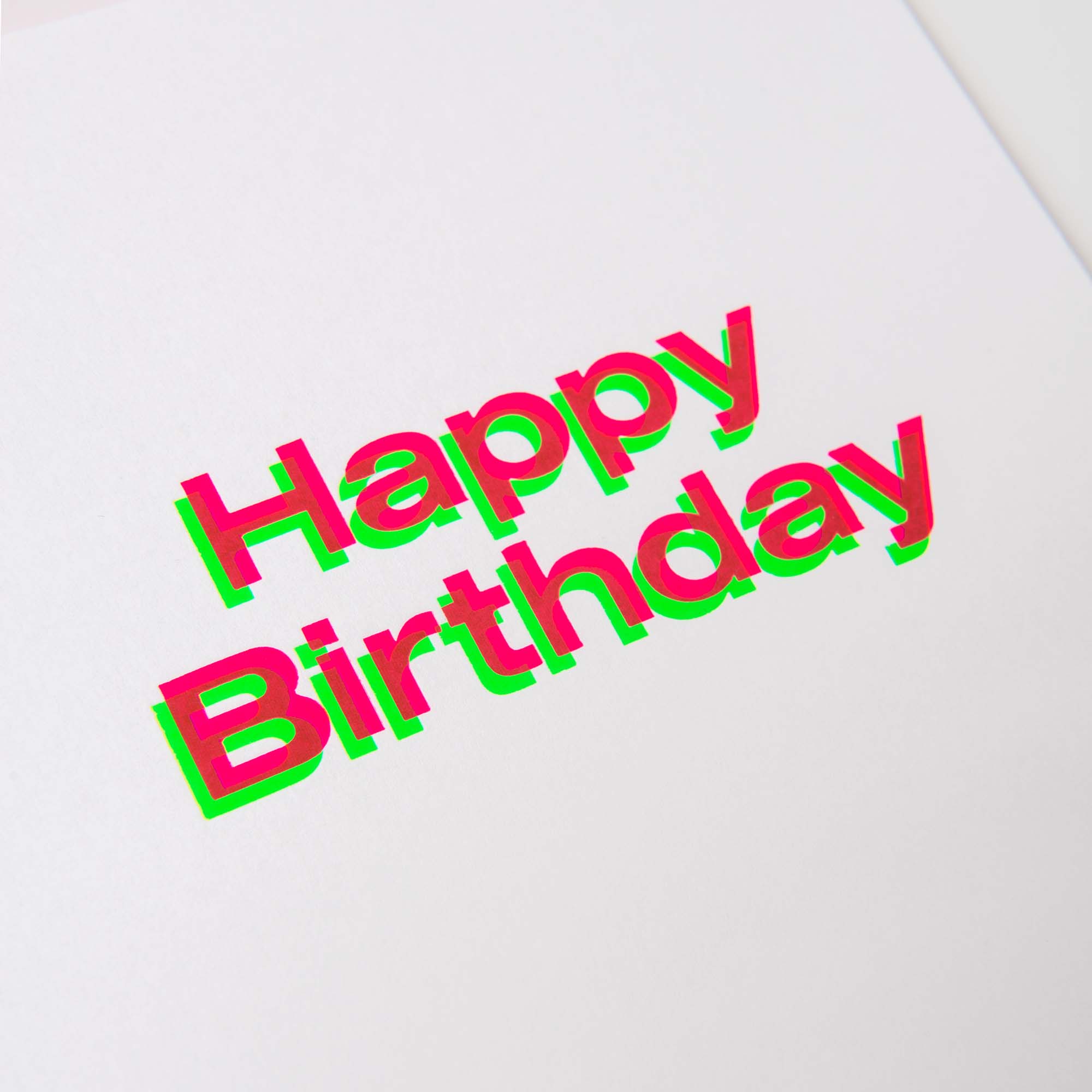Die Happy Birthday Karte A5 von paperlux.store zeigt kräftigen, farbenfrohen 3D-Text mit auffälligen rosa Buchstaben, akzentuiert durch grüne und blaugrüne Schatten auf weißem Hintergrund, der an exquisite Heißfolienprägung erinnert. Ideal für elegante Geburtstagskarten.