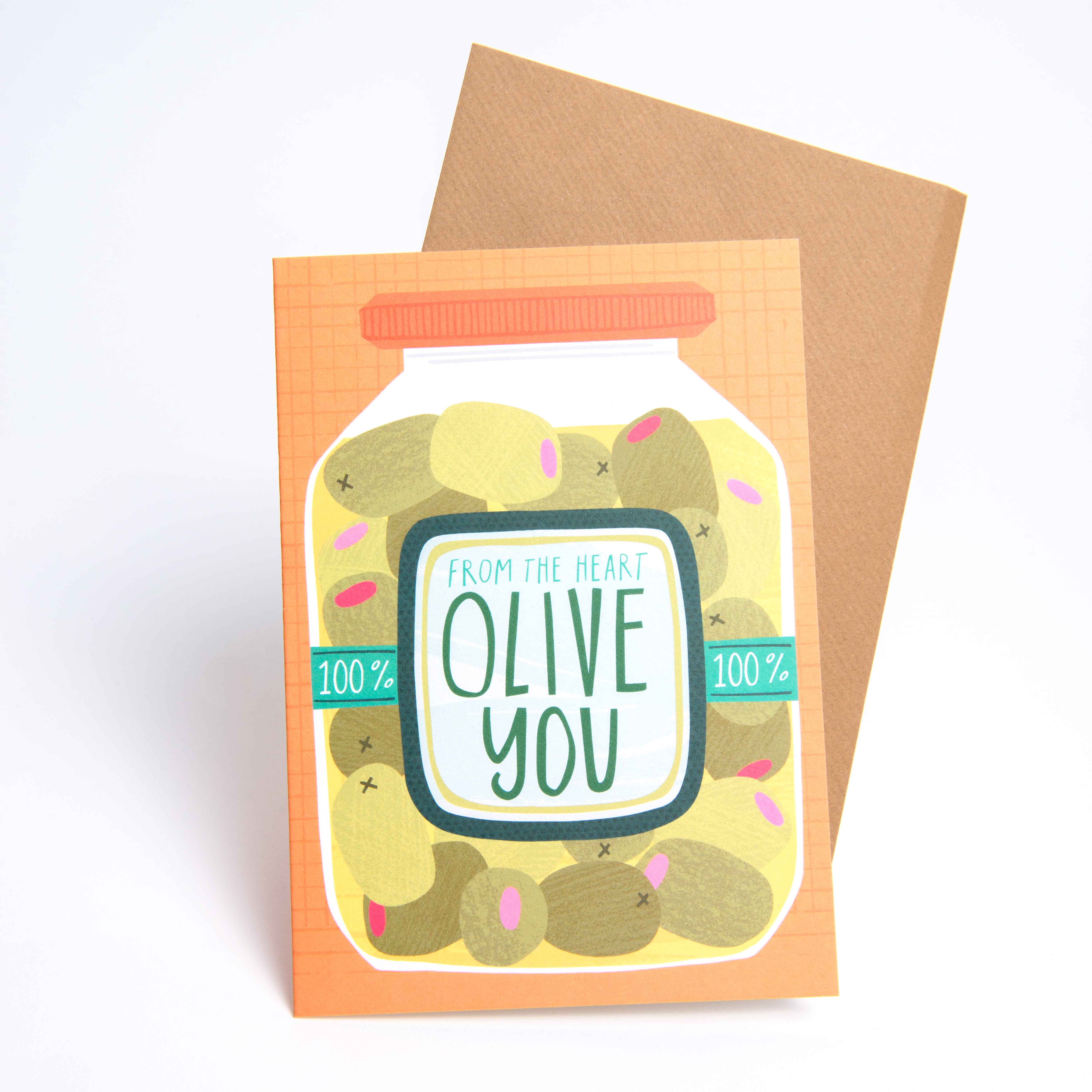 Joanne de Paces „Grußkarte Olive“ zeigt eine Olivenillustration im Glas mit der Aufschrift „Von Herzen, OLIVE YOU“ und einem braunen Umschlag. Eine charmante Ergänzung für Ihre Sammlung, perfekt zum Teilen von Gefühlen rund um Oliven.