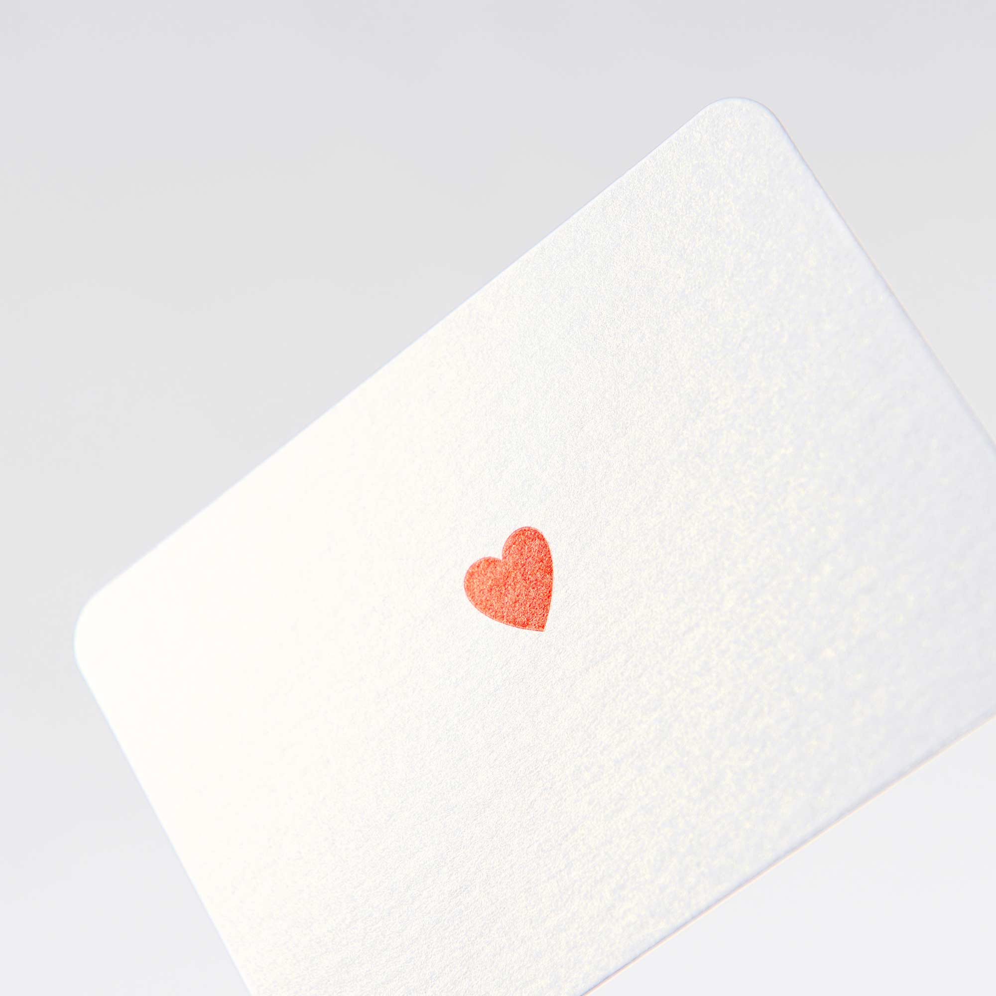 Die Herz - Mini Karte von Le Typographe zeigt ein kleines rotes Herz in der Mitte einer weißen Karte, elegant dargestellt auf einem schlichten weißen Hintergrund. Das leicht geneigte Design strahlt minimalistischen Charme aus und erinnert an die feine Handwerkskunst des Buchdrucks.