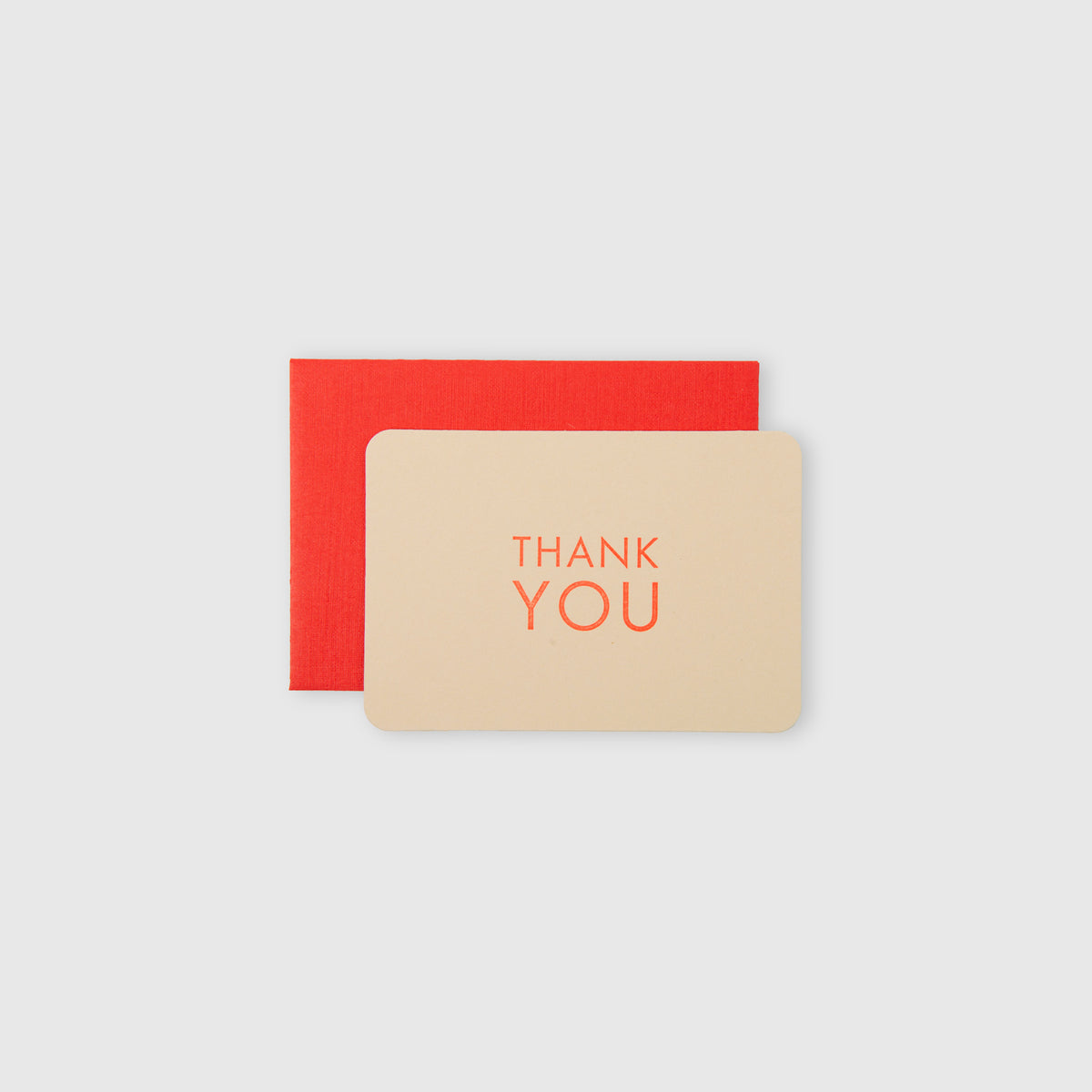 Eine cremefarbene Mini-Karte „Thank You“ – Cappuccino Geranium von Le Typographe, auf der „THANK YOU“ in orangefarbener Schrift im klassischen Buchdruck-Stil aufgedruckt ist, ist auf einem hellgrauen Hintergrund auf einem roten Umschlag abgebildet.