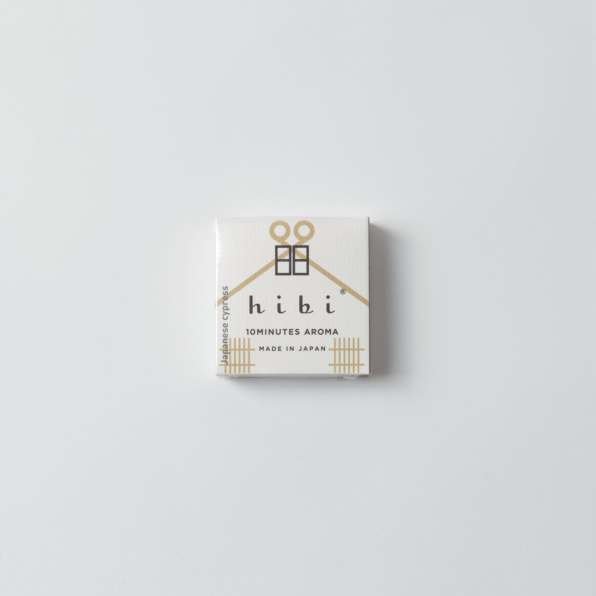 Eine kleine quadratische weiße Box mit minimalistischem Design zeigt den Markennamen „Hibi“ und „10 MINUTES AROMA“ sowie „MADE IN JAPAN“ in Schwarz und Gold. Sie enthält eine hausähnliche Illustration, die die Essenz natürlicher Düfte mit Hibis japanischen Duftstreichhölzern einfängt.