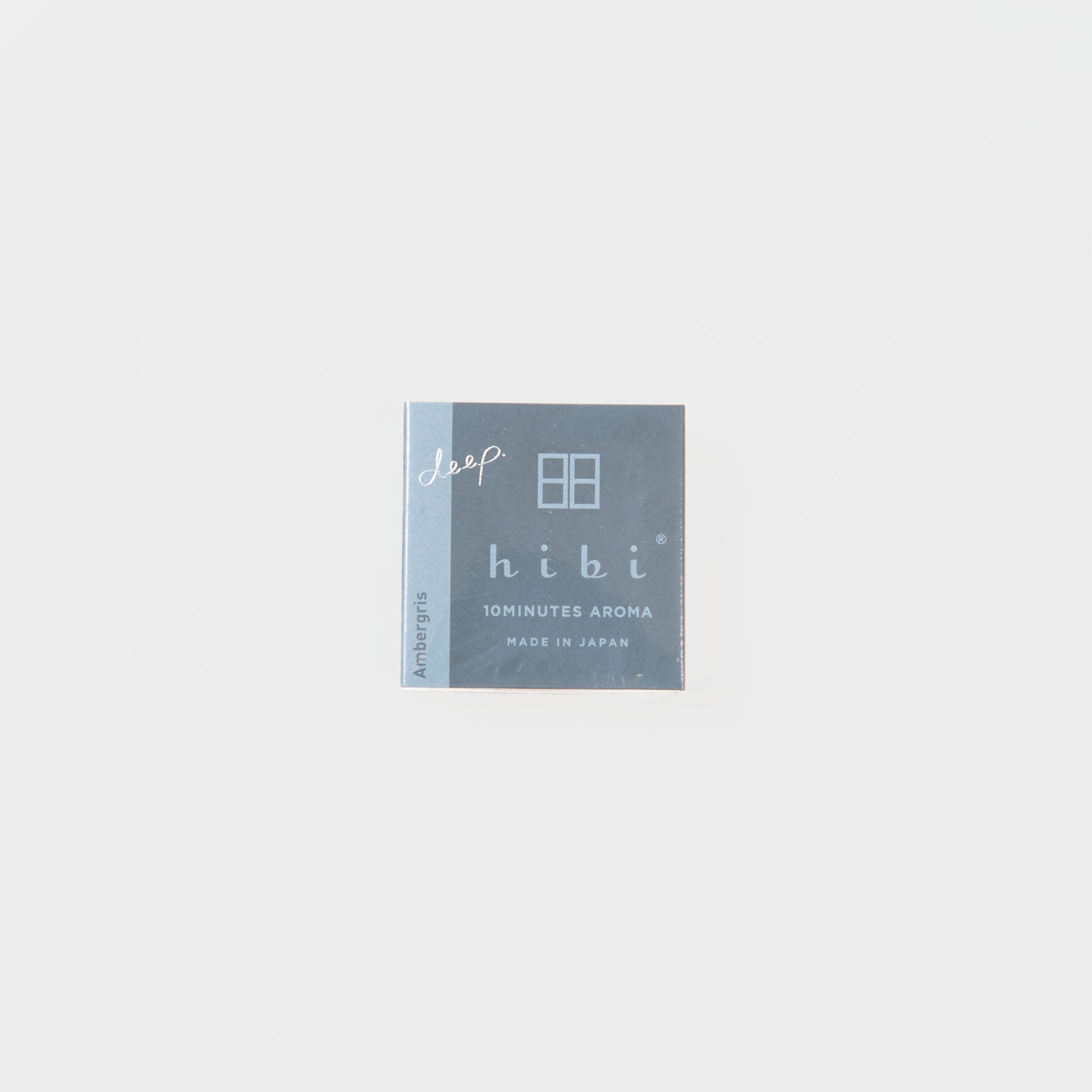 Eine kleine, quadratische, blaugraue Schachtel mit der Aufschrift "Hibi - Duftstreichhölzer" von Hibi, mit "10 MINUTES AROMA MADE IN JAPAN" und "Ambergris", die an japanische Streichhölzer erinnert, steht mittig auf einem schlichten weißen Hintergrund.