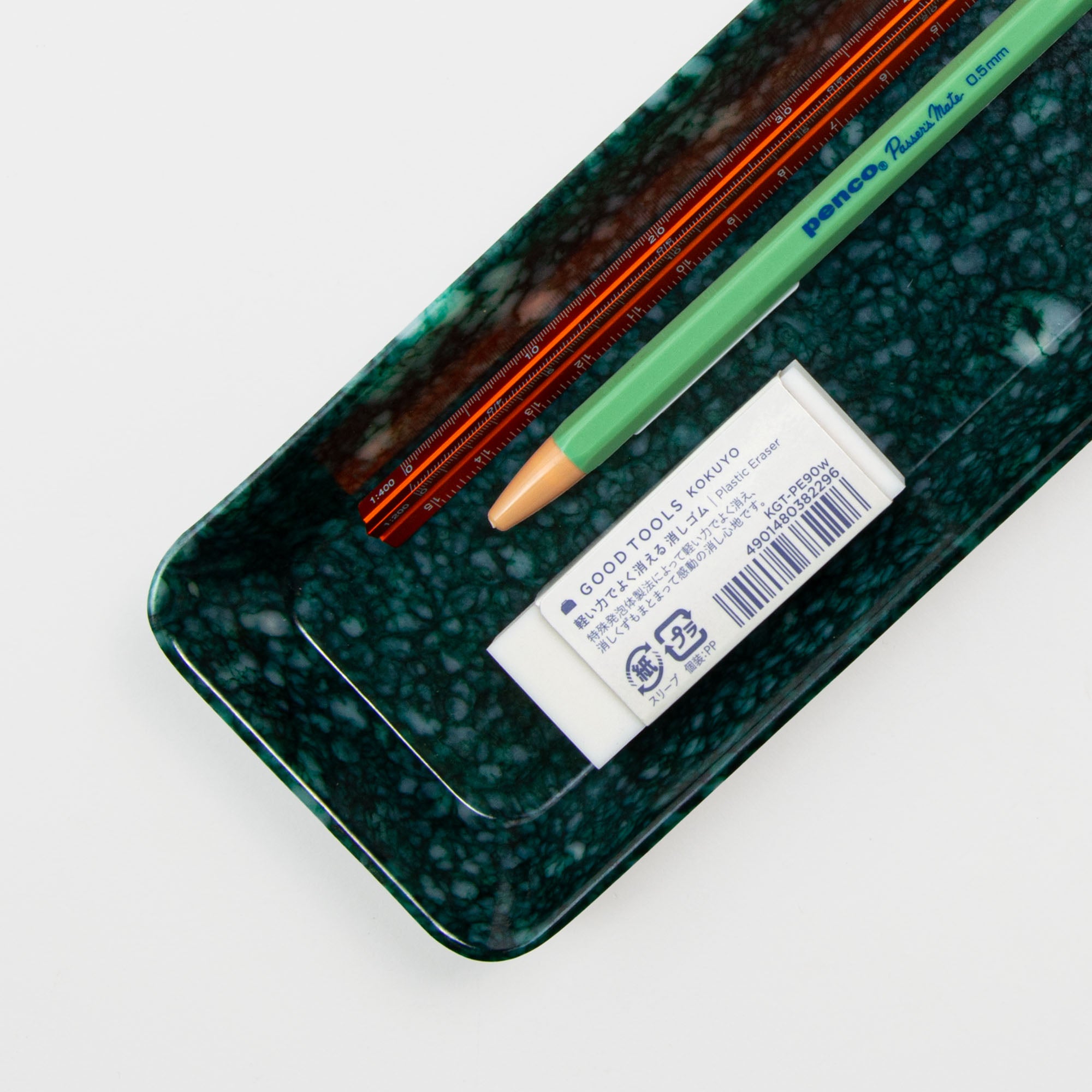 Das Pen Tray Dark Green von Hightide enthält zwei orangefarbene Bleistifte, einen grünen Kugelschreiber und einen weißen rechteckigen Radiergummi mit der Aufschrift GOODTOOLS KOKUYO, die alle ordentlich auf einem weißen Hintergrund angeordnet sind.
