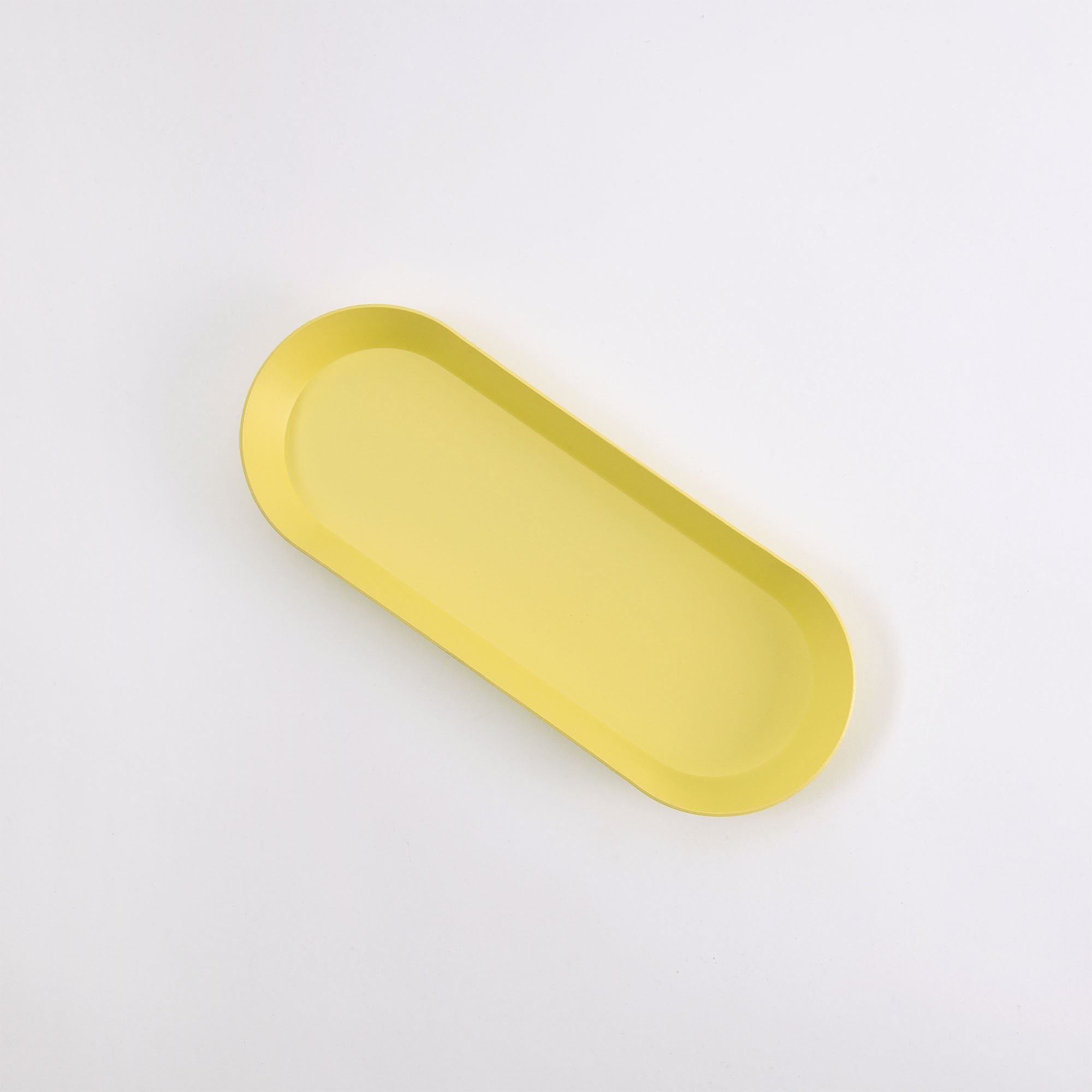 Eine Ovale Schale von Hightide in gelber ovaler Form mit leicht erhöhten Rändern präsentiert sich elegant auf weißem Hintergrund.